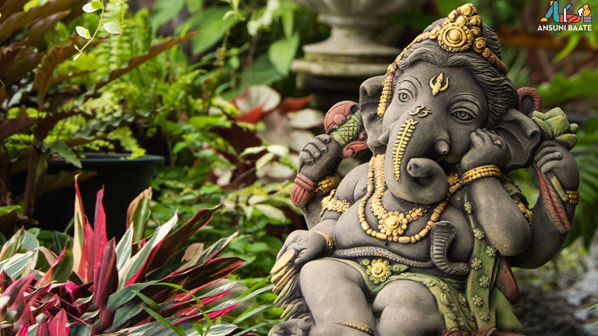 Ganesh 桌布 壁紙 — 一尊精緻的象神石像，飾以黃金珠寶，安詳地坐落在茂密的熱帶植物和鮮豔的紅綠色植物之間。