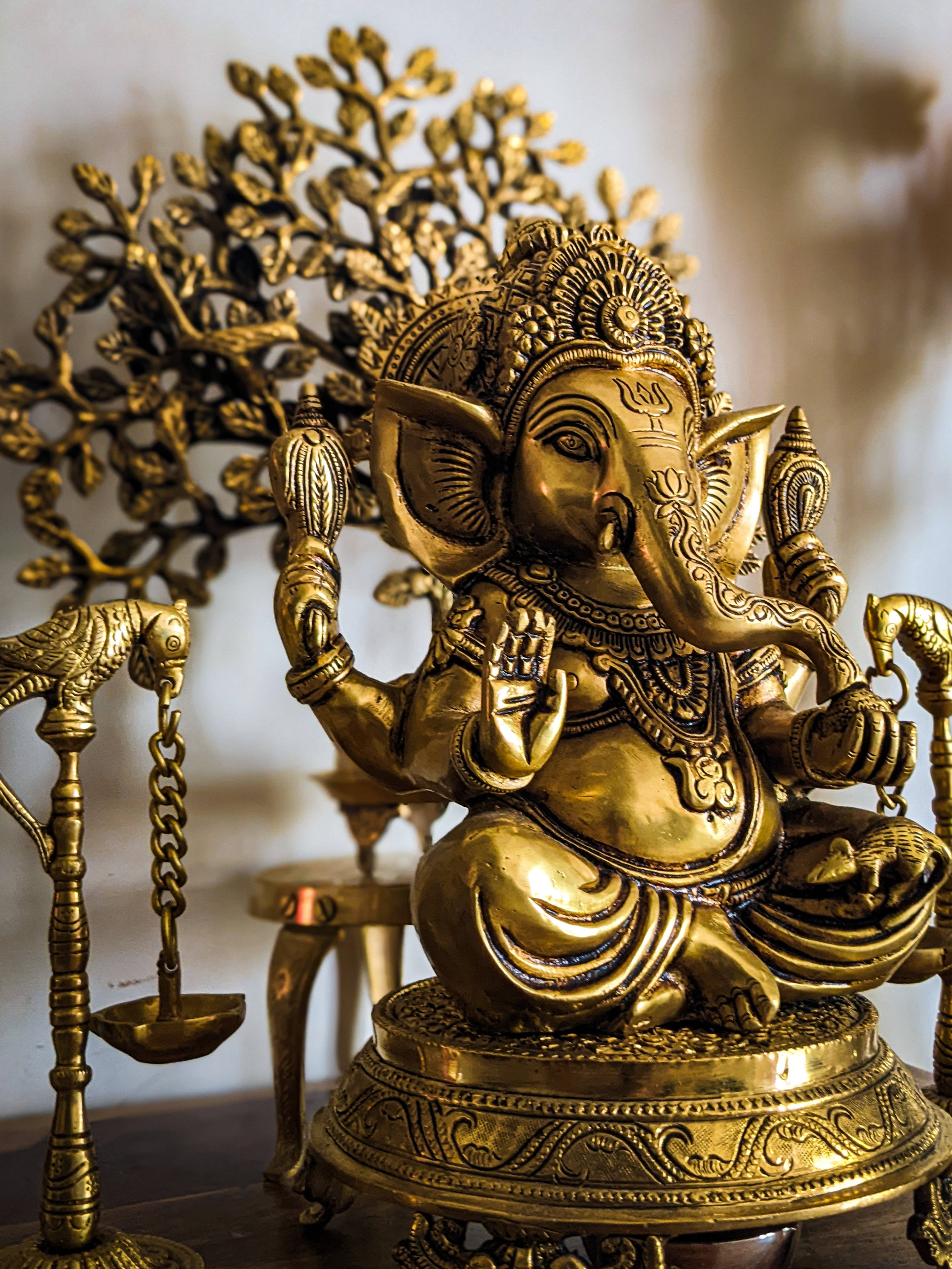 ganesh 4K 桌布 壁紙 — 一尊精緻的金色象神雕像威嚴地坐在華麗的基座上，周圍環繞著相配的黃銅儀式物品。