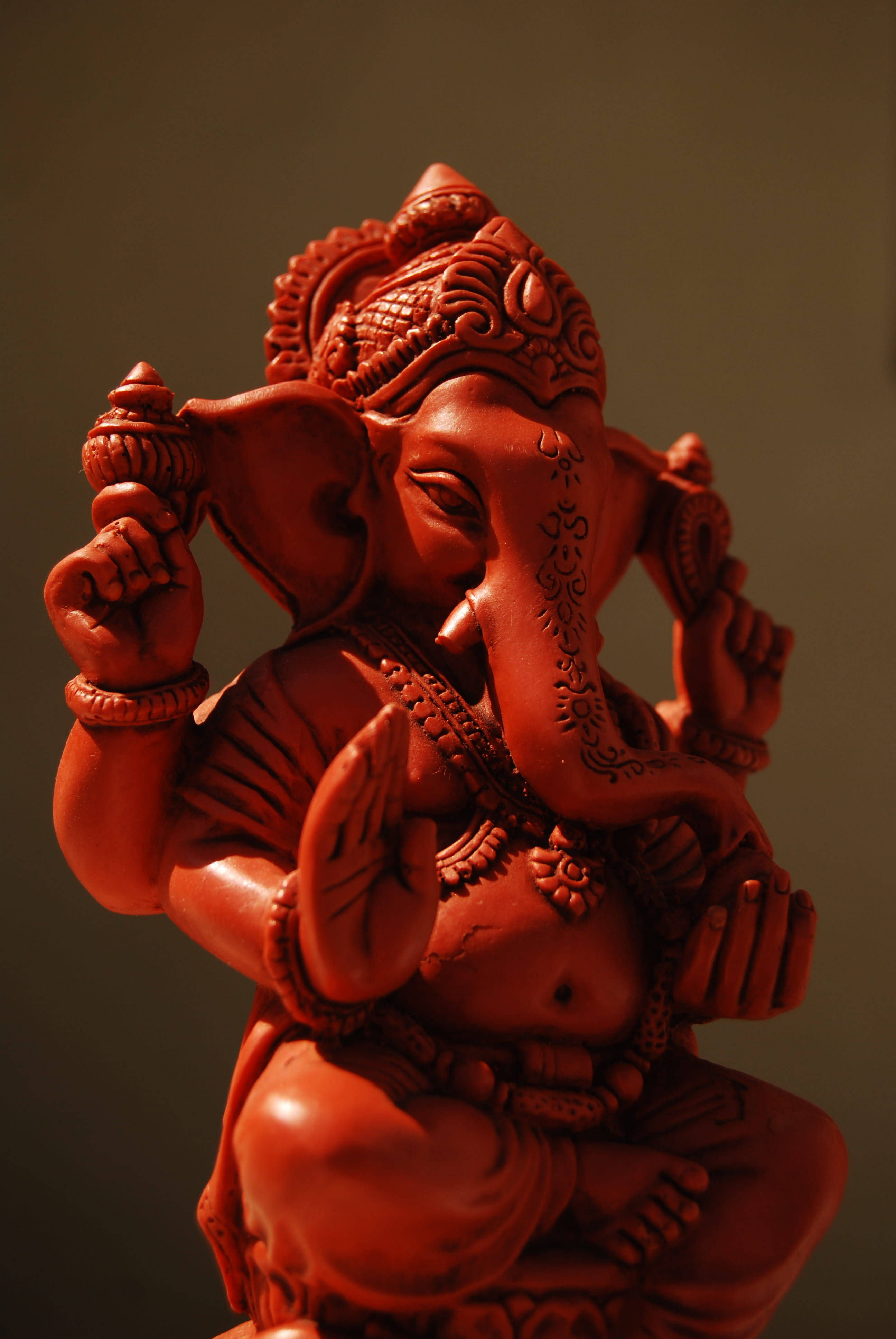 ganesh iPhone 桌布 壁紙 — 一尊細節豐富的紅色赤陶象頭神像，雕刻精緻，在溫暖燈光下表情寧靜。
