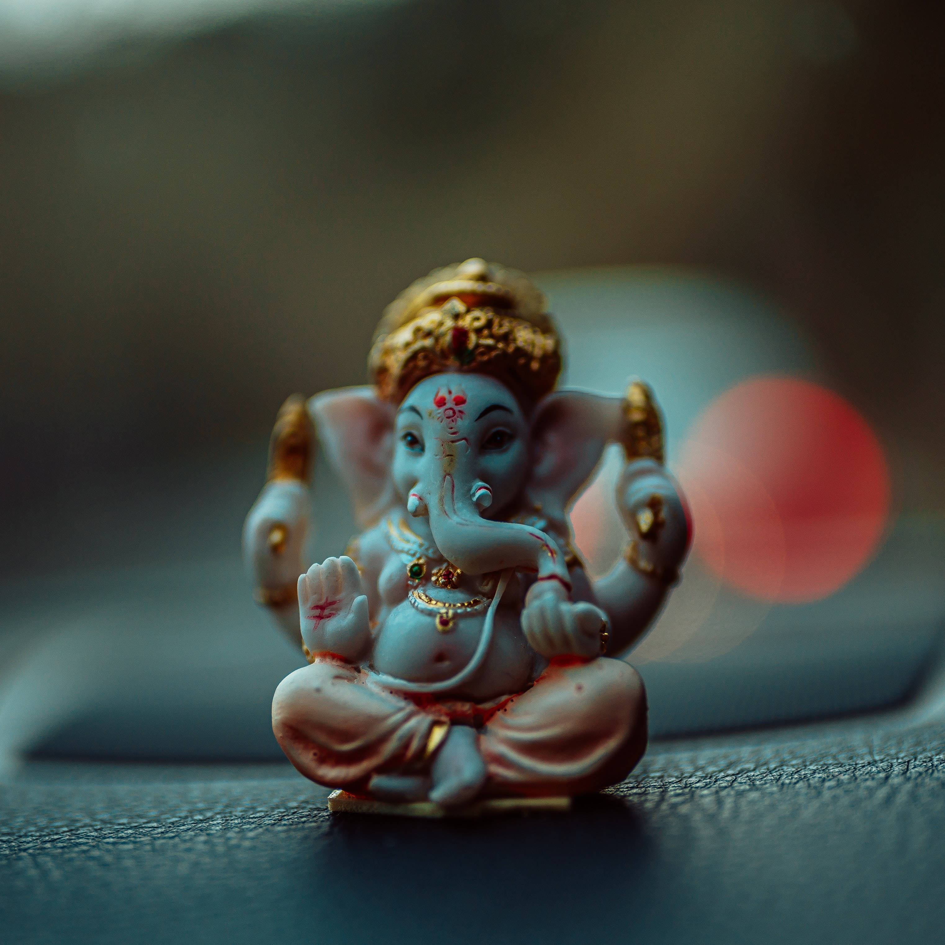 Ganesh 桌布 壁紙 — 一尊細節豐富的象頭神像安詳地坐在有紋理的表面上，背景是柔和散景燈光。