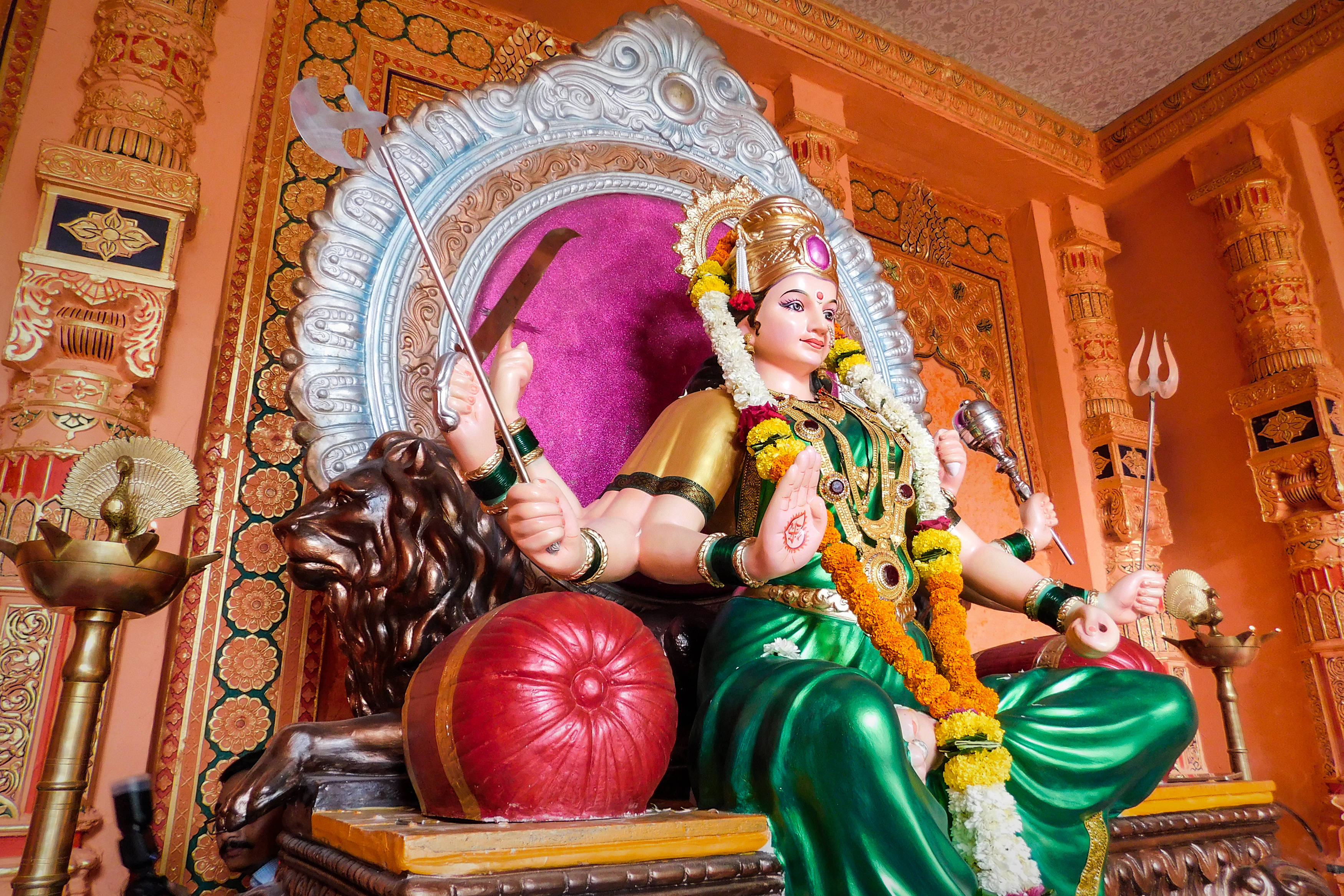 Navratri 桌布 壁紙 — 一尊色彩鮮豔、多臂的印度教女神雕像，身披綠色與金色，莊嚴地坐在華麗寺廟內的獅子寶座上。