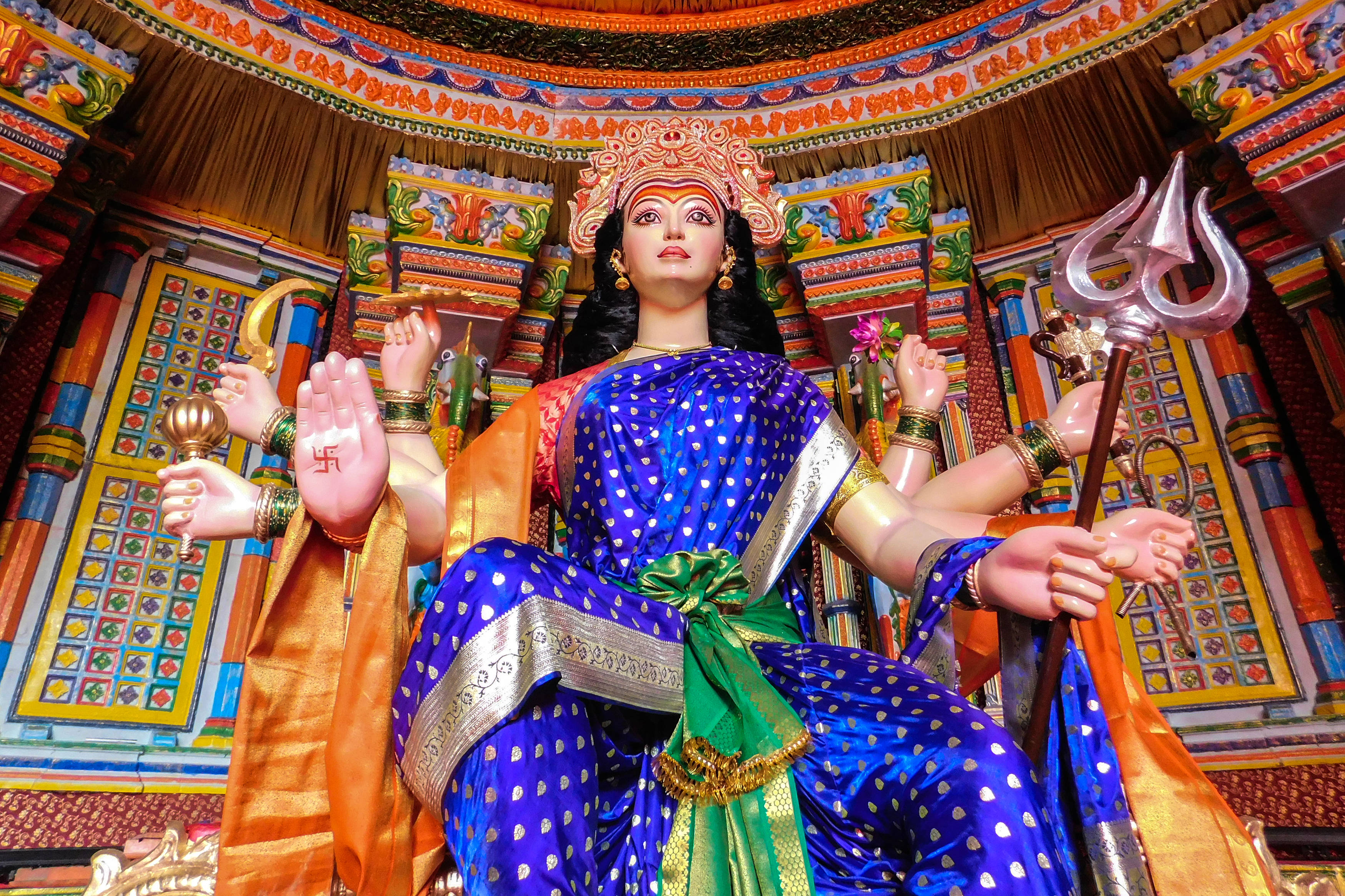 Navratri 桌布 壁紙 — 一尊色彩鮮豔的印度教女神杜爾迦雕像，以藍色和金色裝飾，多臂手持武器，坐在裝飾華麗的寺廟神龕中。