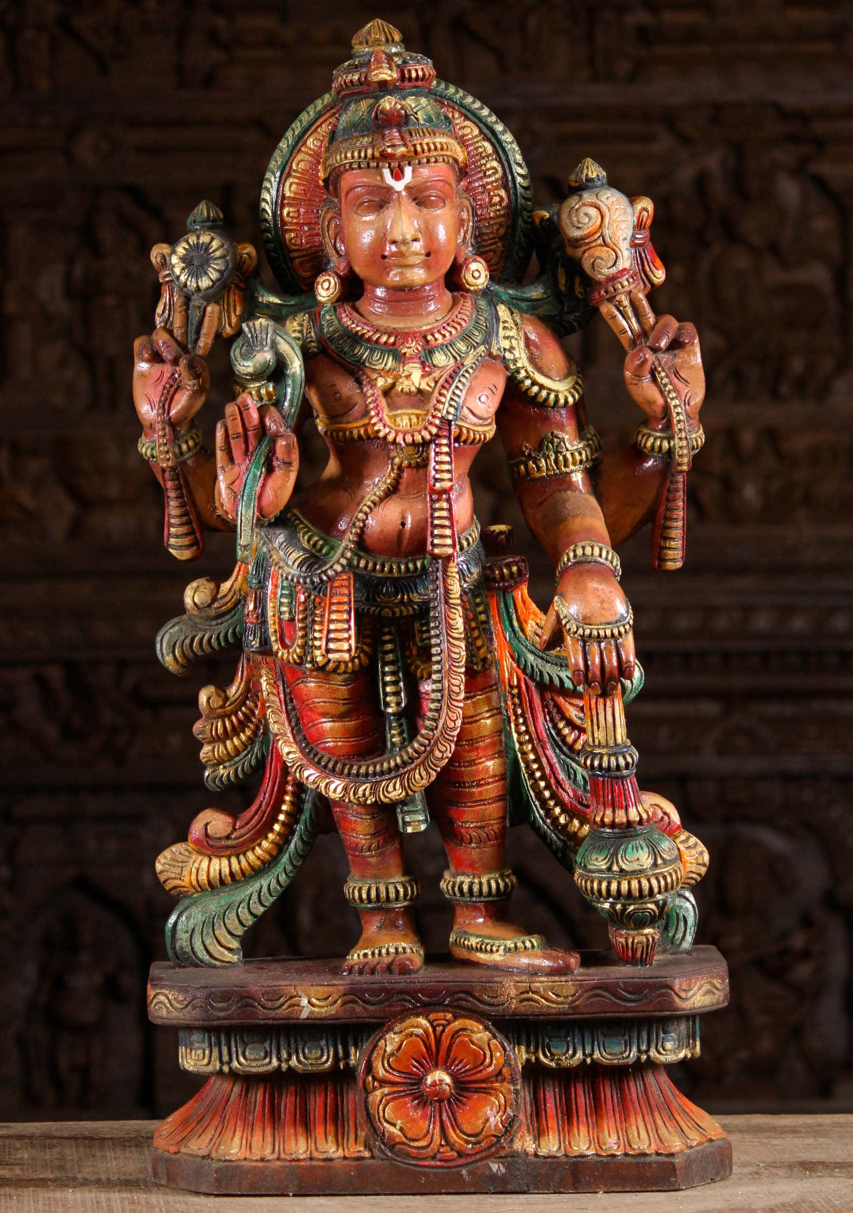 Indian God 桌布 壁紙 — 一尊色彩鮮豔的多臂印度教神祇木雕神像，威嚴地矗立在裝飾華麗的基座上，背景是雕刻的木製屏風。