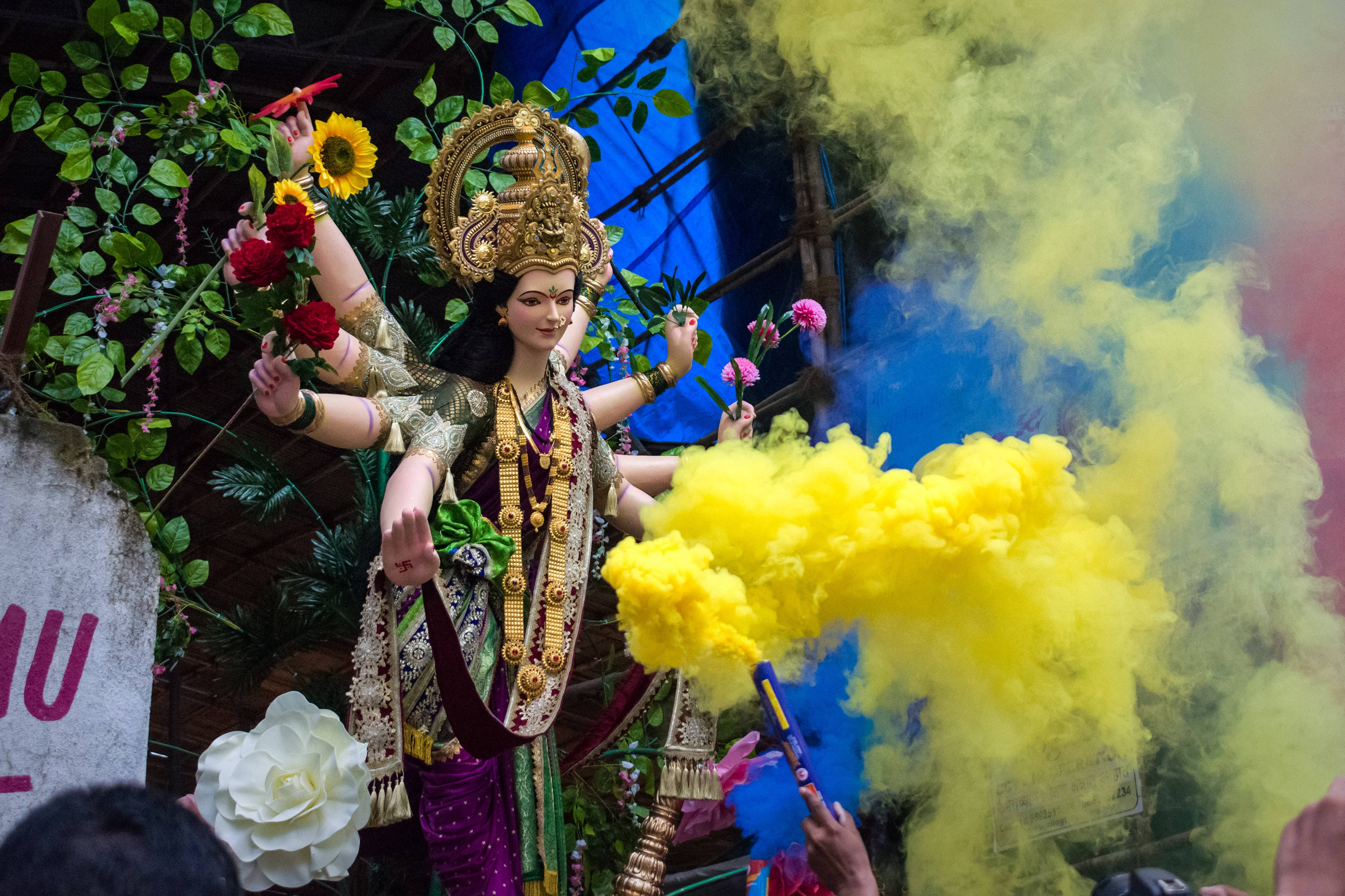 Mata Rani 桌布 壁紙 — 一尊色彩鮮豔的多臂女神雕像，飾有黃金珠寶和鮮花，在節日慶祝活動中矗立於五彩煙霧之中。