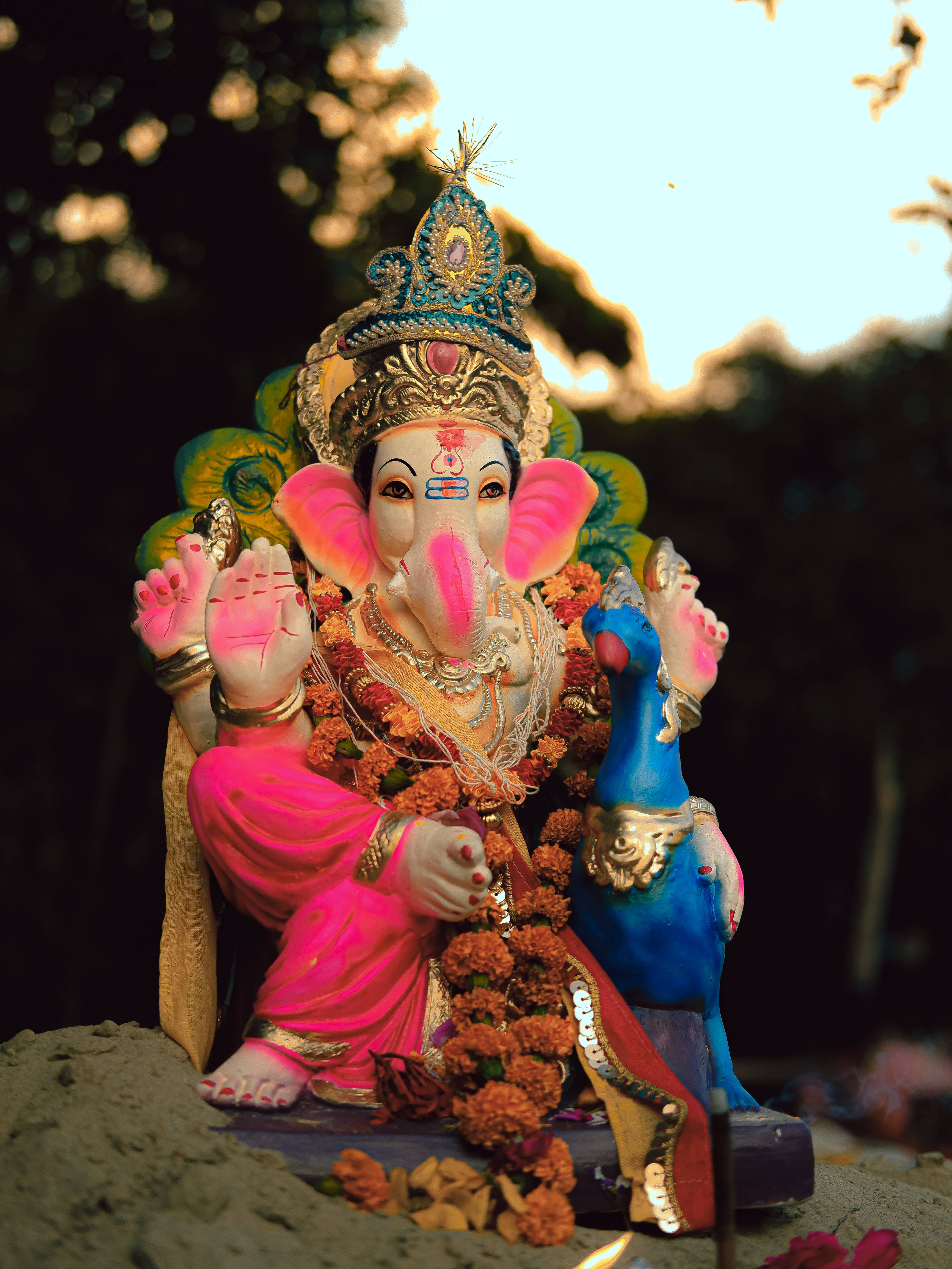 Ganesh Chaturthi 桌布 壁紙 — 一尊色彩鮮豔的象神像，飾有鮮花和珠寶，在黃金時刻寧靜地坐在戶外。