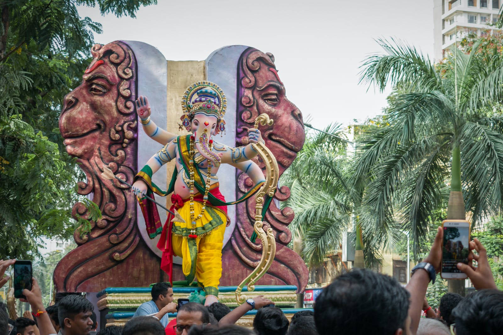 Ganesh 桌布 壁紙 — 一尊色彩鮮豔的象神像矗立在裝飾華麗的花車上，信徒們簇擁著捕捉節慶時刻。