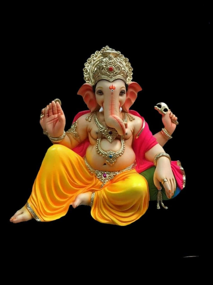 Ganesh 桌布 壁紙 — 一尊色彩鮮豔的象神迦尼薩雕像，盤腿坐在黑色背景前，佩戴金色珠寶和紅黃色腰布，手持摩達克和斧頭。