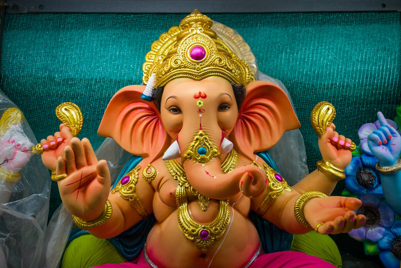 Vinayaka 桌布 壁紙 — 一尊色彩鮮豔的象頭神像，飾有黃金珠寶和鑲有寶石的王冠，莊嚴地坐在青綠色背景前。