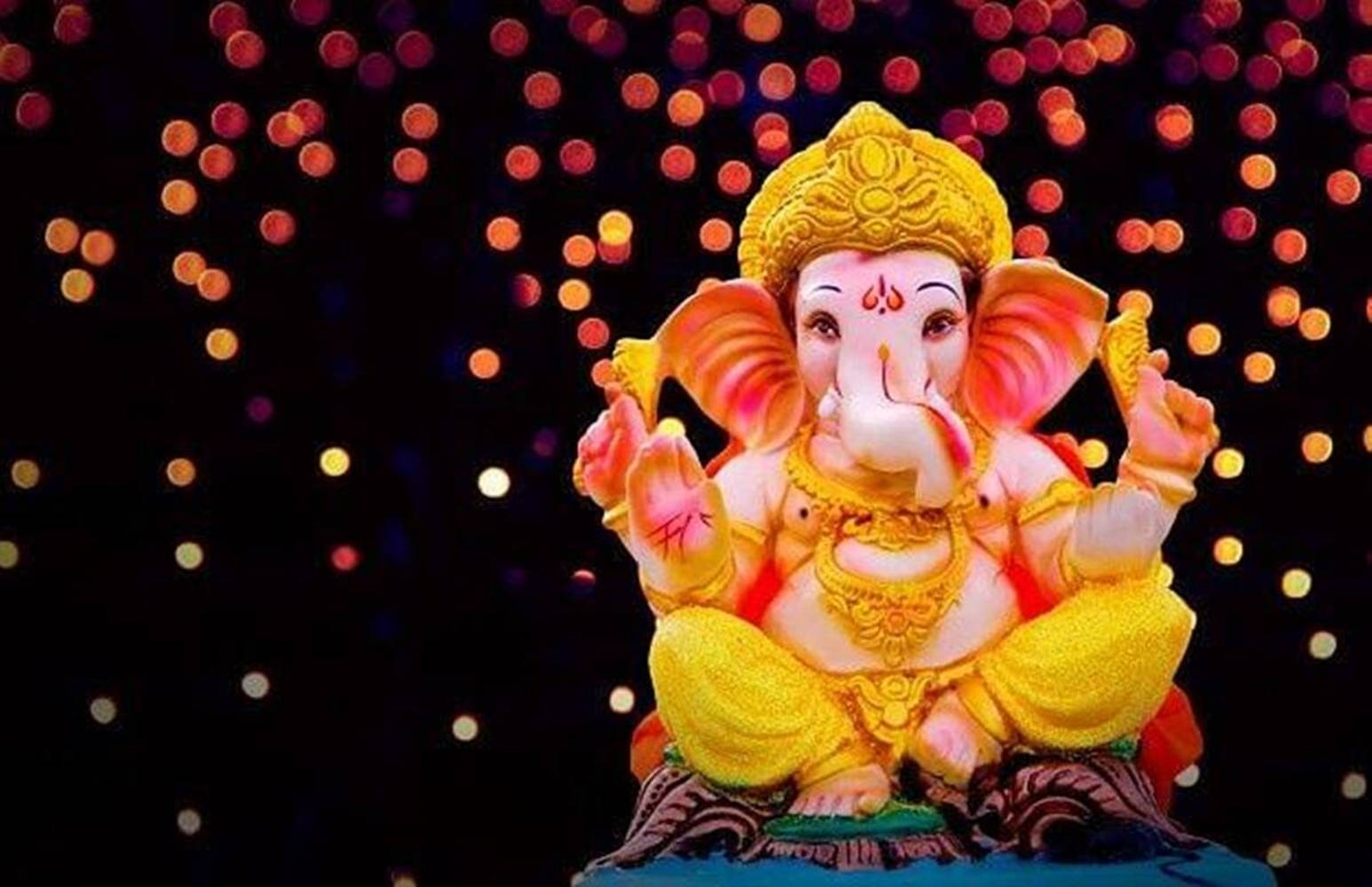 Ganesh 桌布 壁紙 — 一尊色彩鮮豔的象頭神像在閃爍的散景燈光背景下靜靜地坐著。