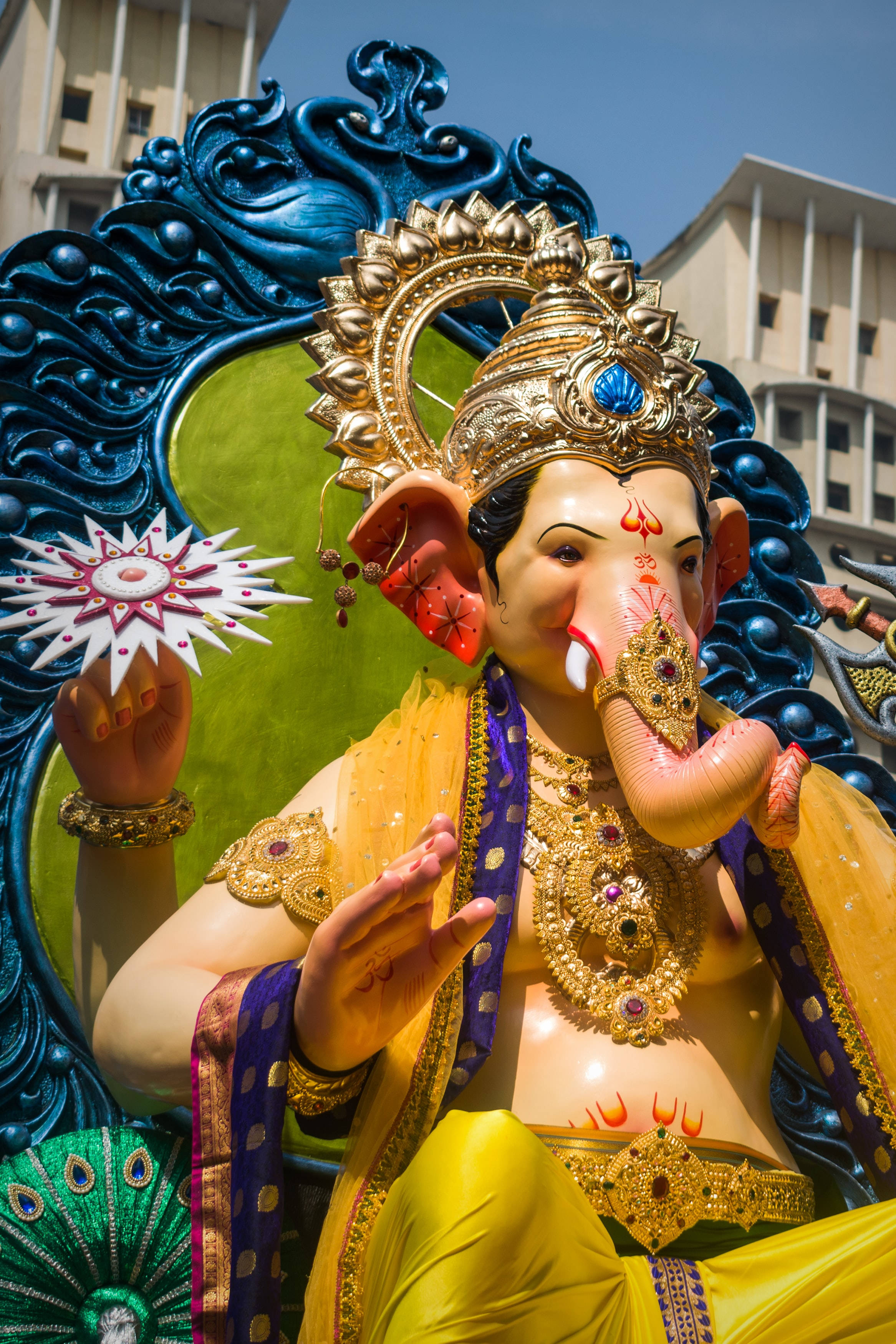 Hindu Temple 桌布 壁紙 — 一尊色彩鮮豔的金色象神像，飾有珠寶，並以藍色華麗框架襯托城市背景。