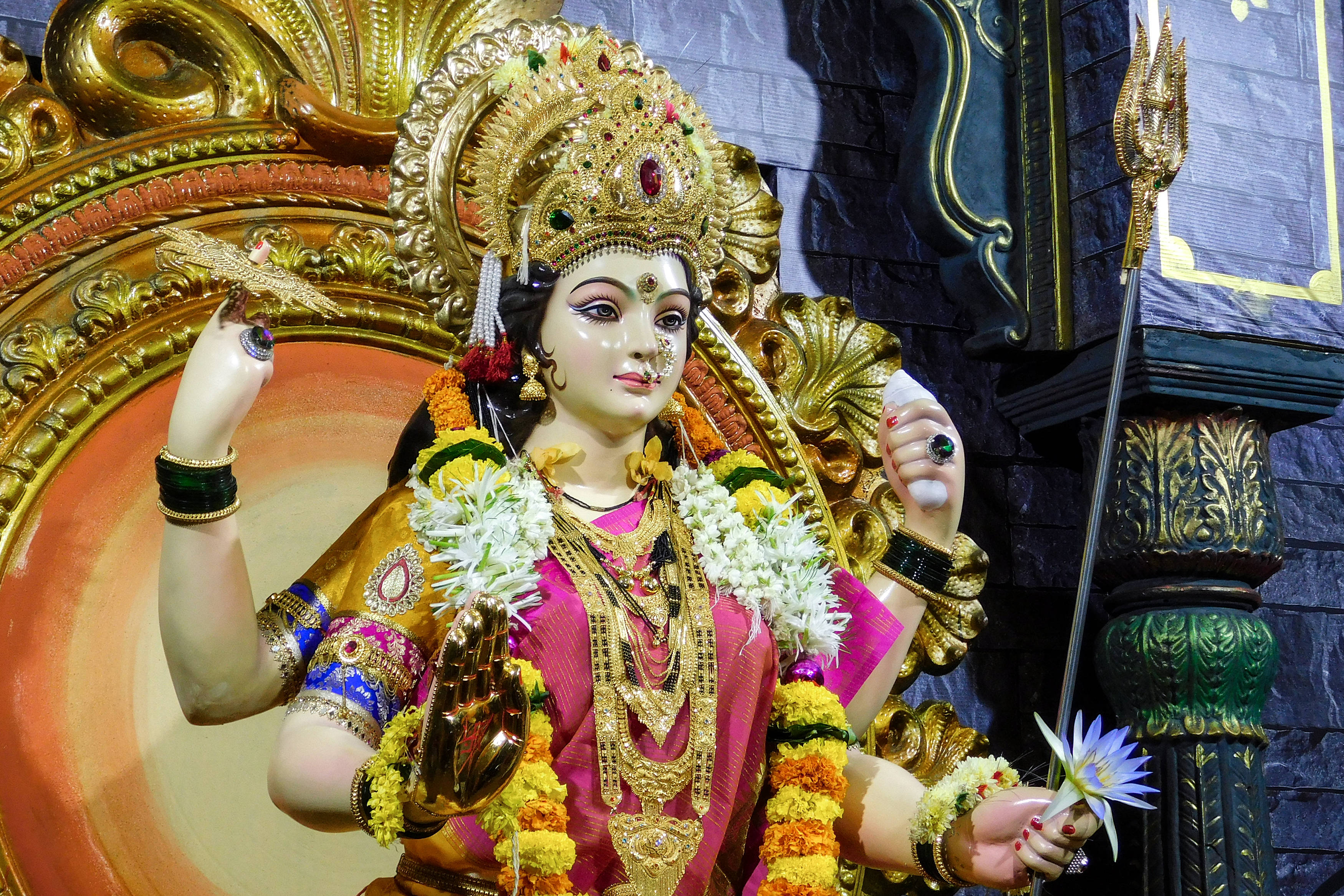 Navratri 桌布 壁紙 — 一尊色彩鮮豔的黃金杜爾迦女神像，飾有鮮花和珠寶，手持武器，背景是裝飾華麗的寺廟。