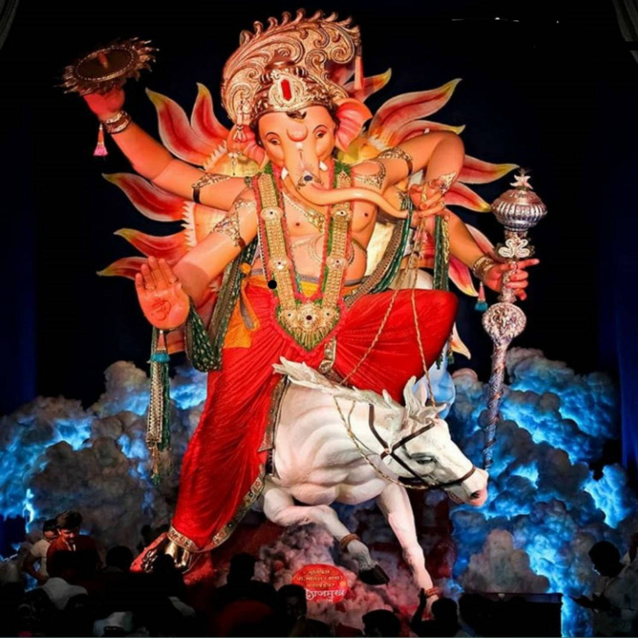 ganpati HD 桌布 壁紙 — 一尊莊嚴的多臂象神像，身穿鮮豔的紅色和金色長袍，騎著白馬，背景是發光的藍色雲彩。