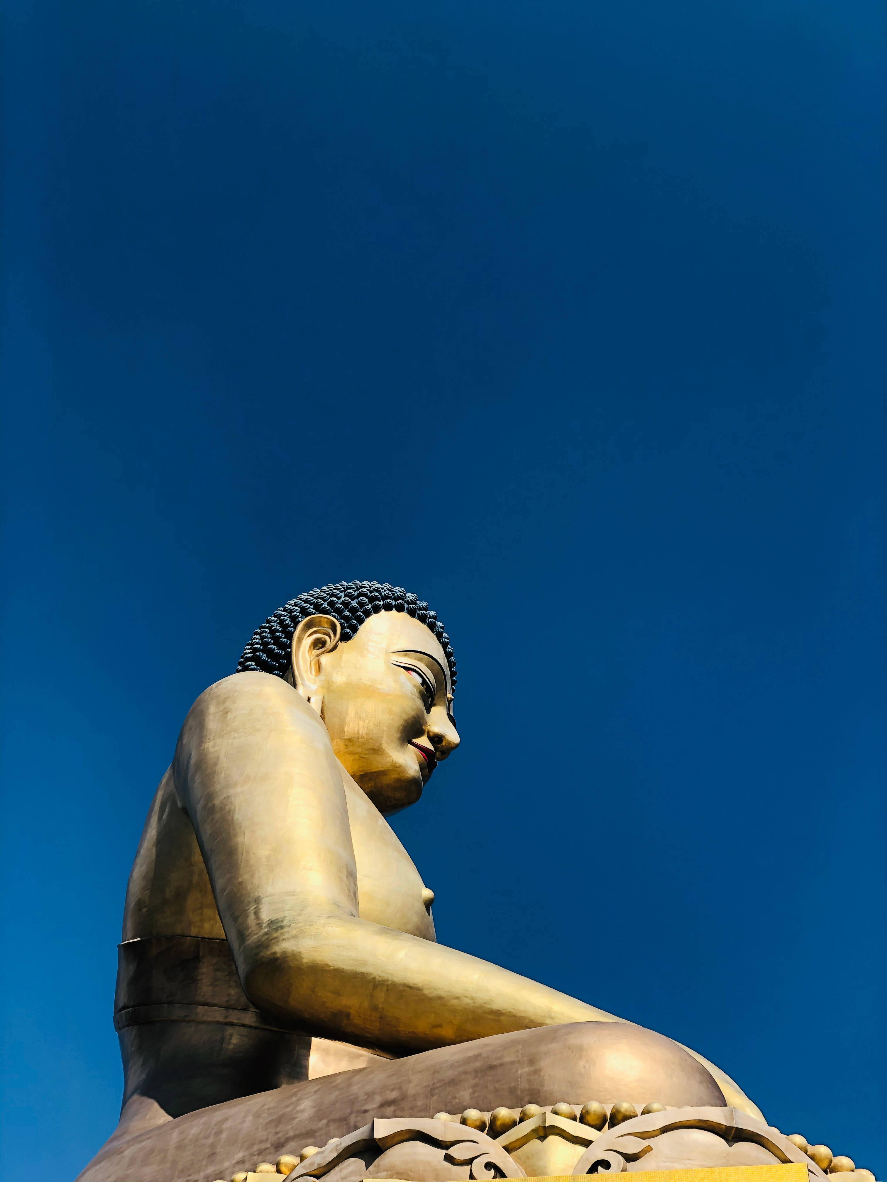 Bhutan 桌布 壁紙 — 一尊莊嚴的金色佛像在深藍色的天空下靜坐，散發出平靜和精神的存在。