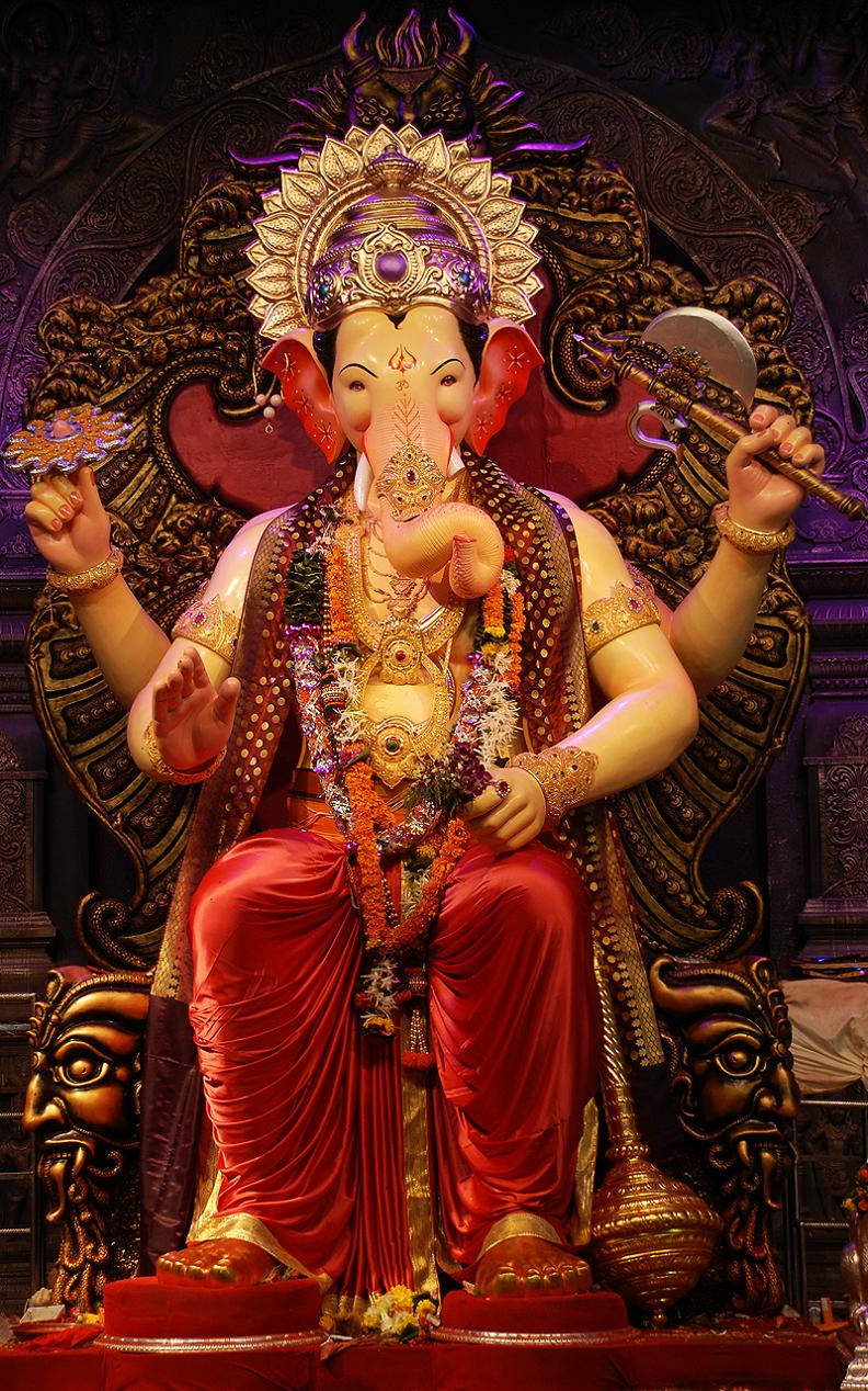 Hindu Temple 桌布 壁紙 — 一尊莊嚴的金色象神迦尼薩雕像，坐在裝飾華麗的寶座上，寶座覆蓋著紅色布料，並飾有精緻珠寶和花環。