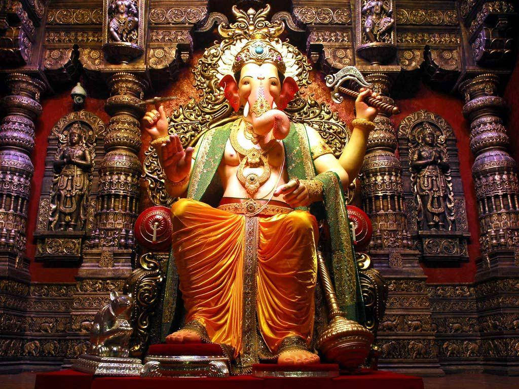 Hindu Temple 桌布 壁紙 — 一尊莊嚴的金色象神迦尼薩雕像，坐在裝飾華麗、雕刻精緻的寶座上，並披有鮮豔的橙色布料。