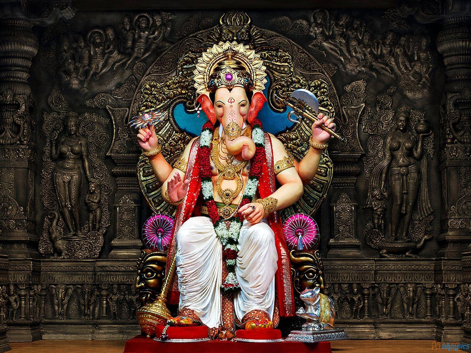 Ganesh 桌布 壁紙 — 一尊莊嚴的金色象神雕像，飾以紅色花環和珠寶，端坐在華麗的寶座上，背景是暗色雕刻的寺廟。