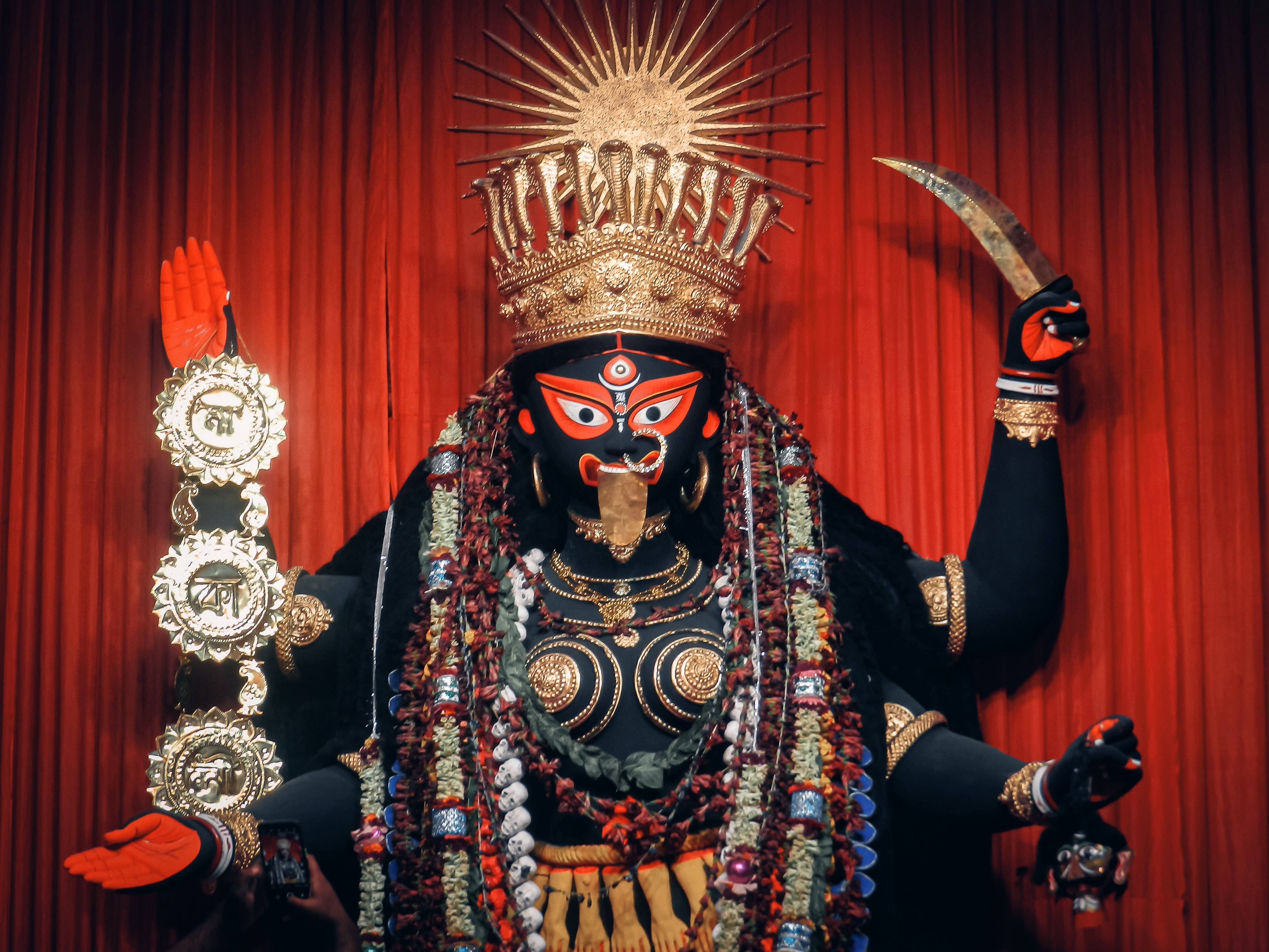 Goddess 桌布 壁紙 — 一尊莊嚴的黑臉女神雕像，飾有金色王冠珠寶和彩色珠子，站在深紅色窗簾前。