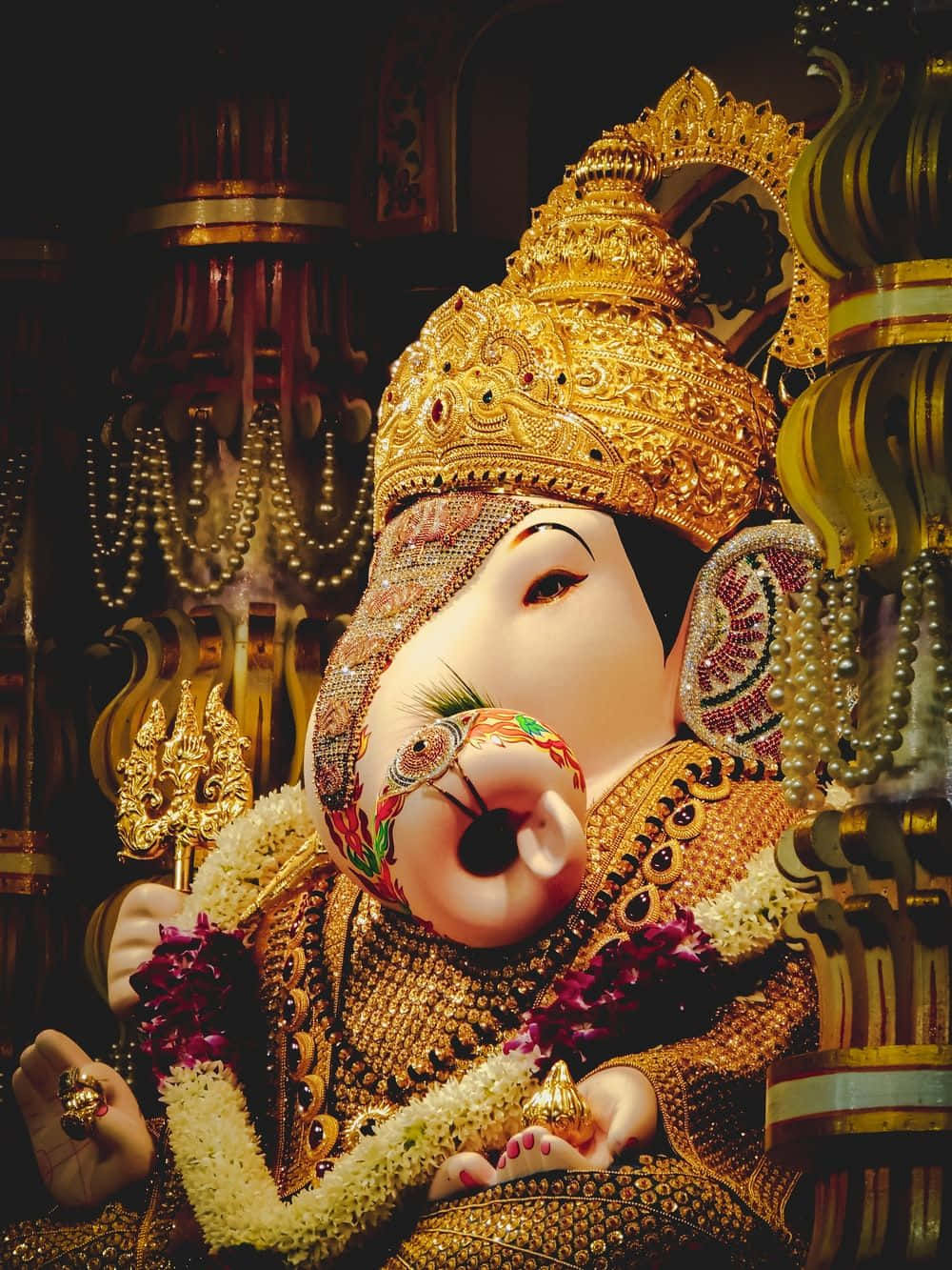 Ganesh 桌布 壁紙 — 一尊華麗裝飾的金色象神雕像，戴著珠寶皇冠和花環，在溫暖的燈光下閃耀。