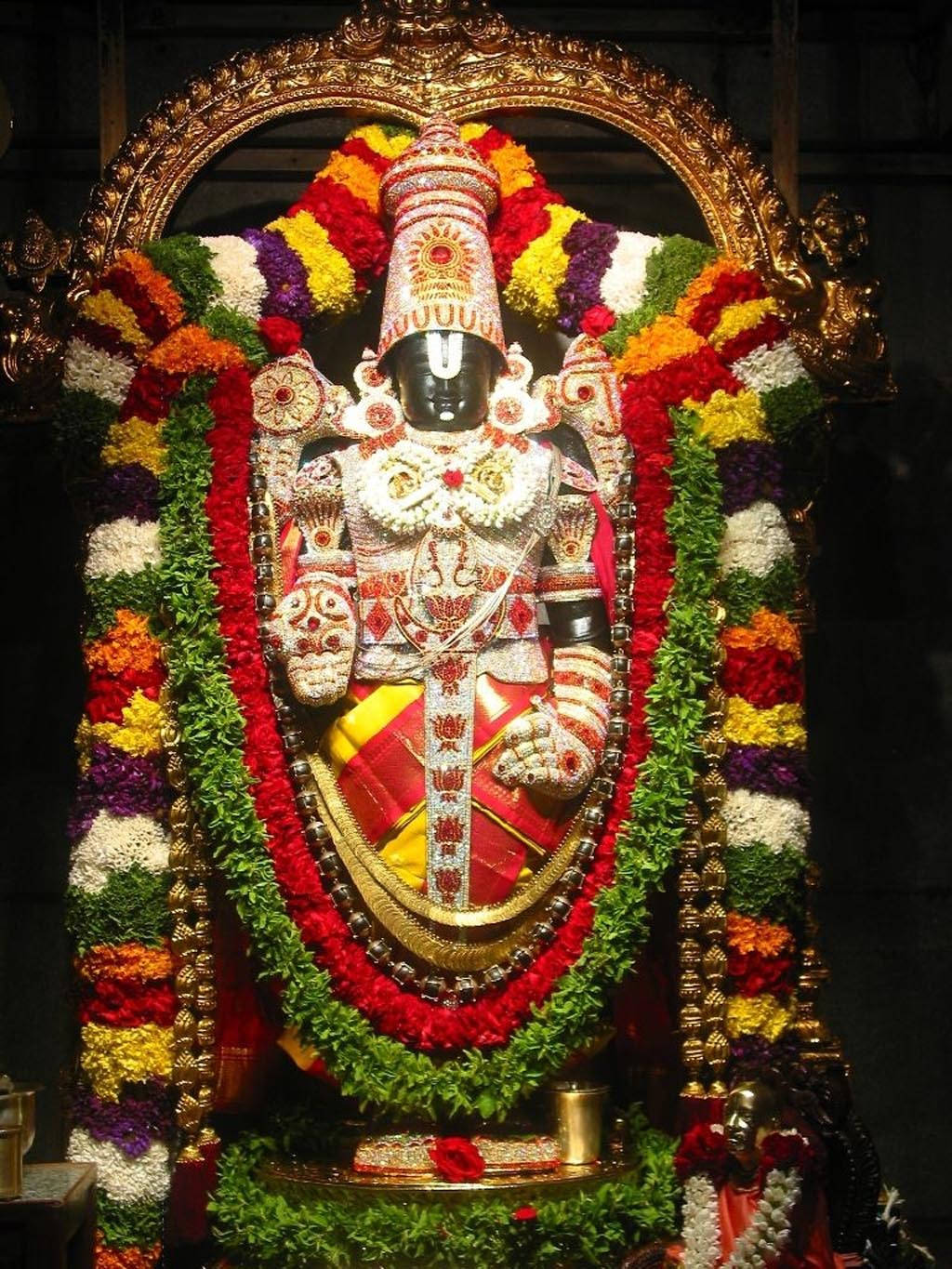 Indian 桌布 壁紙 — 一尊裝飾華麗的印度教神像，披著鮮豔的花環和金飾，在戲劇性的燈光下。