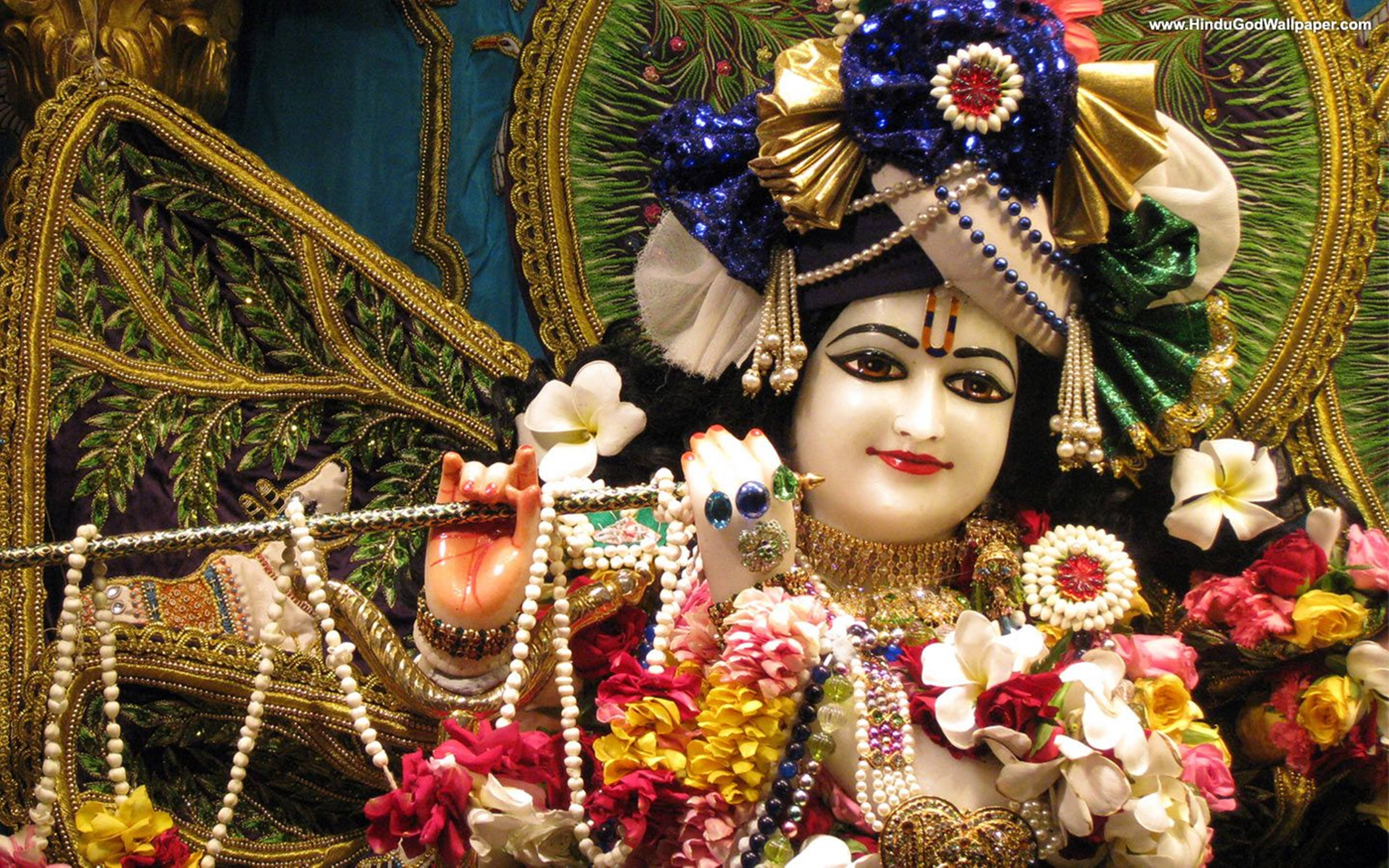 Krishna Flute 桌布 壁紙 — 一尊裝飾華麗的印度教神像，頭戴鑲有寶石的皇冠，身披花環，莊嚴地坐在華麗的金色和綠色背景前。