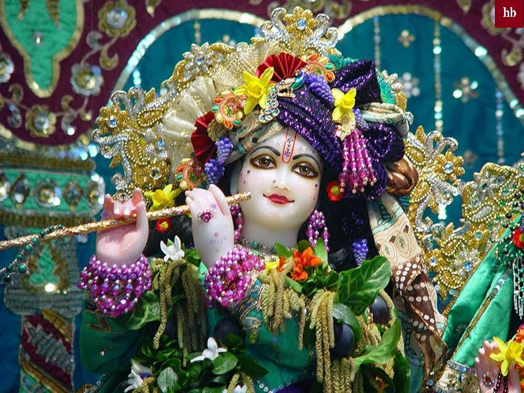 krishna bhagwan 桌布 壁紙 — 一尊裝飾華麗的神像，戴著鑲有寶石的皇冠和花環，在閃閃發光的藍綠色和金色背景下吹奏長笛。