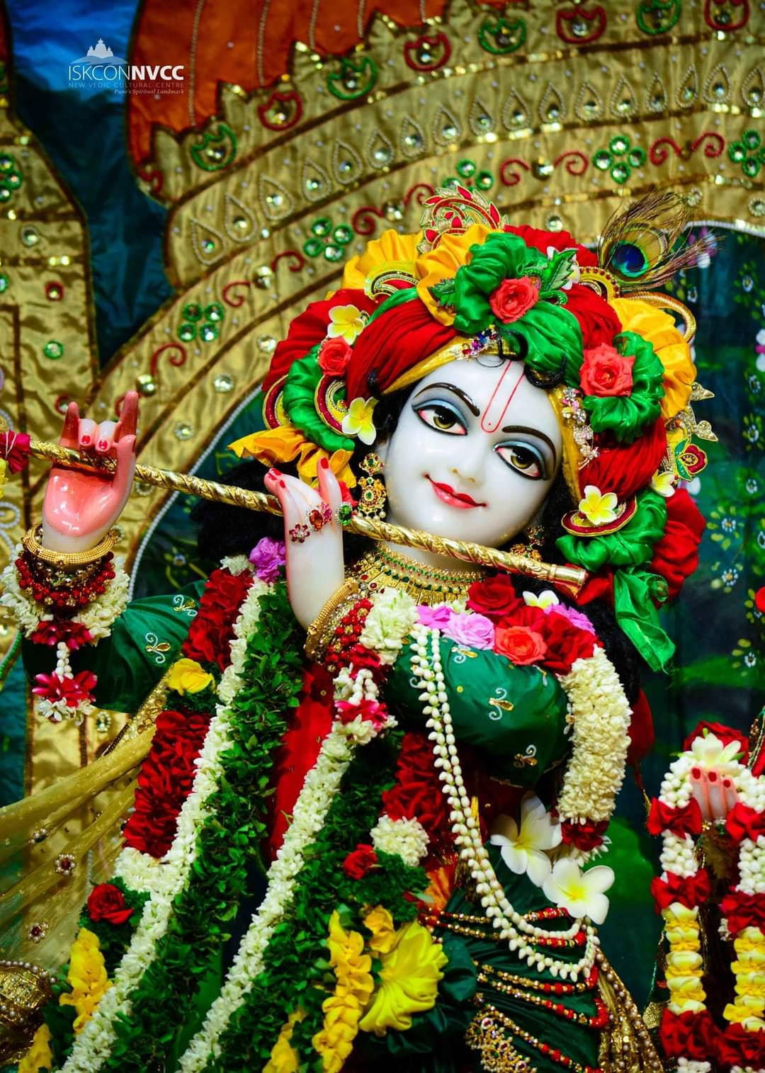 krishna god 桌布 壁紙 — 一尊裝飾華麗的神像，頭戴花冠、身披花環，在鑲滿寶石的金色背景下吹奏長笛。