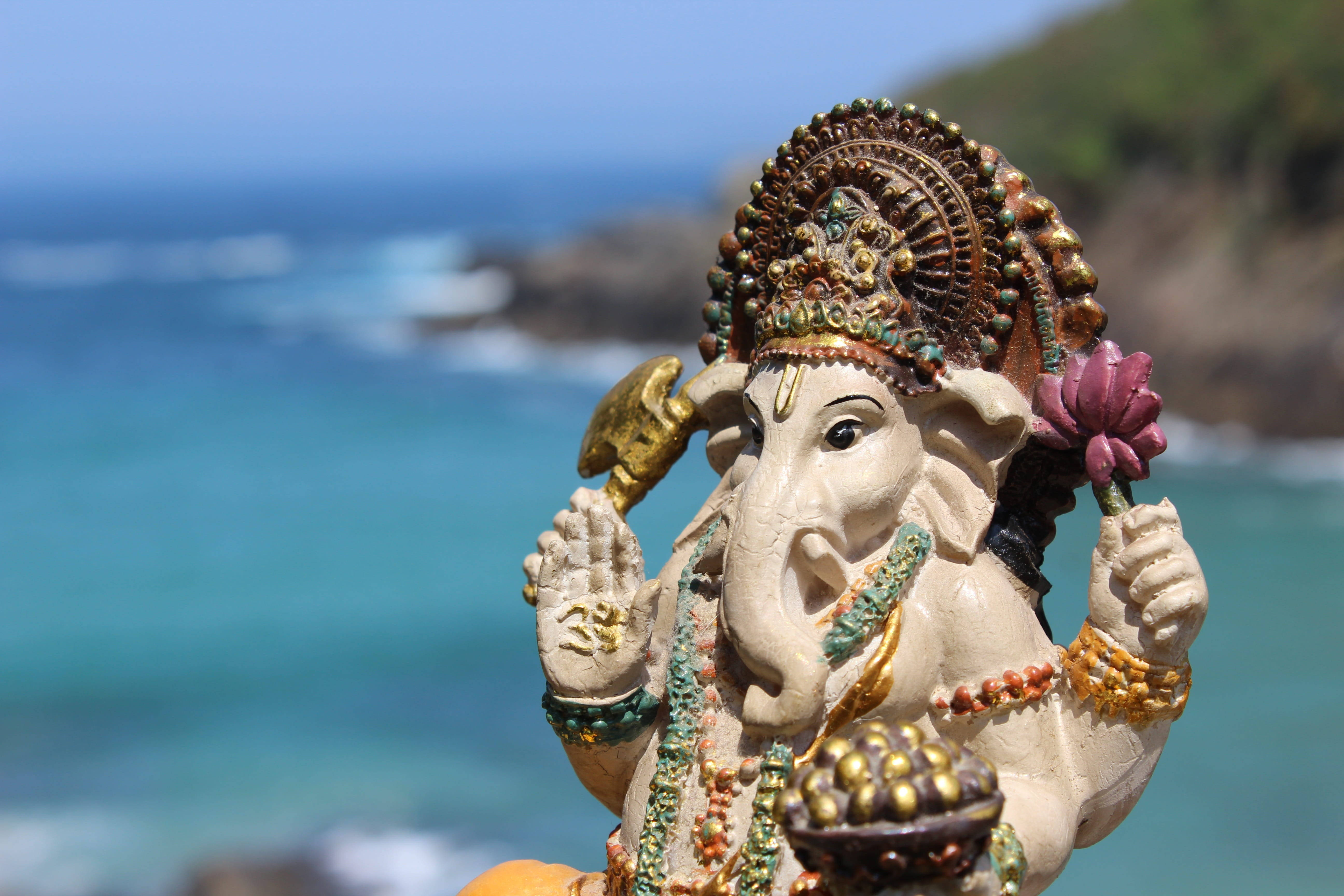 Ganesh 桌布 壁紙 — 一尊裝飾著黃金和珠子的詳細象神雕像，以模糊的綠松石海洋為背景。