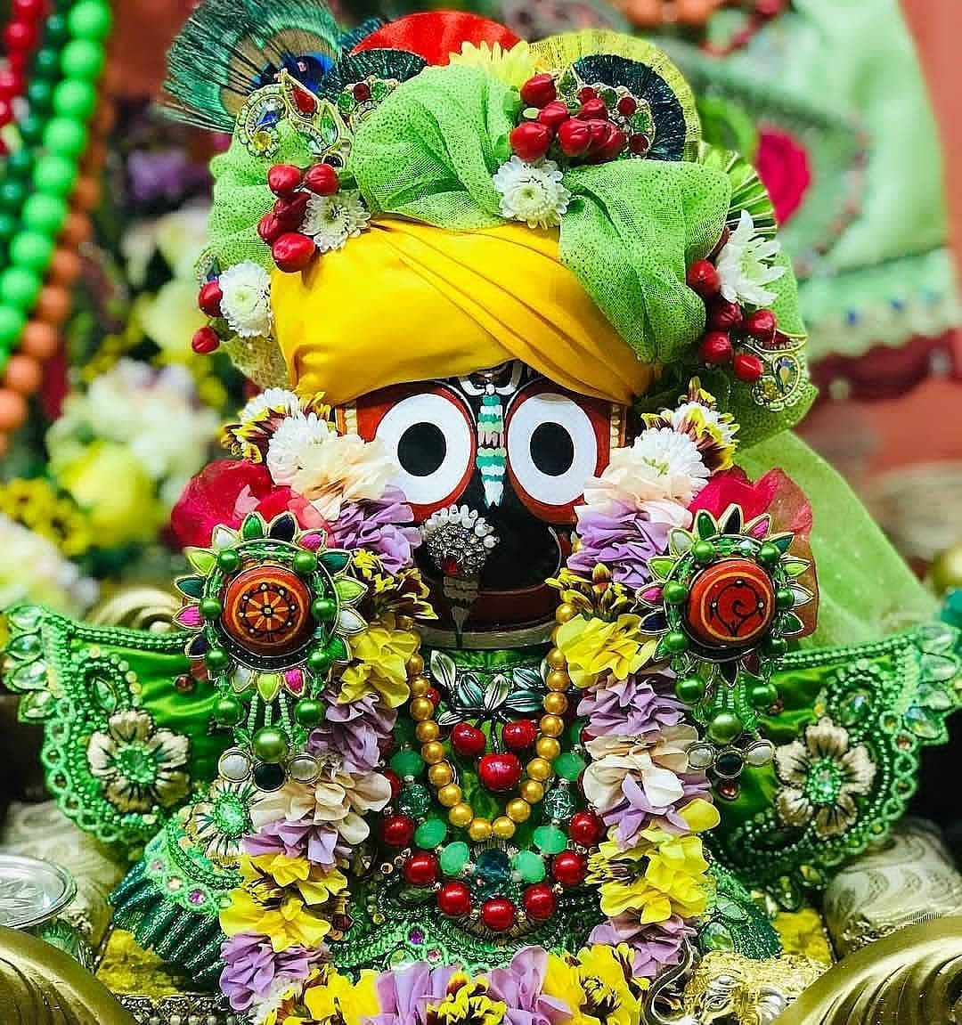Jagannath 桌布 壁紙 — 一尊裝飾鮮豔的印度教神像，有著白色大眼睛，戴著黃色頭巾，並以綠色花朵珠子和彩色飾品華麗裝飾。