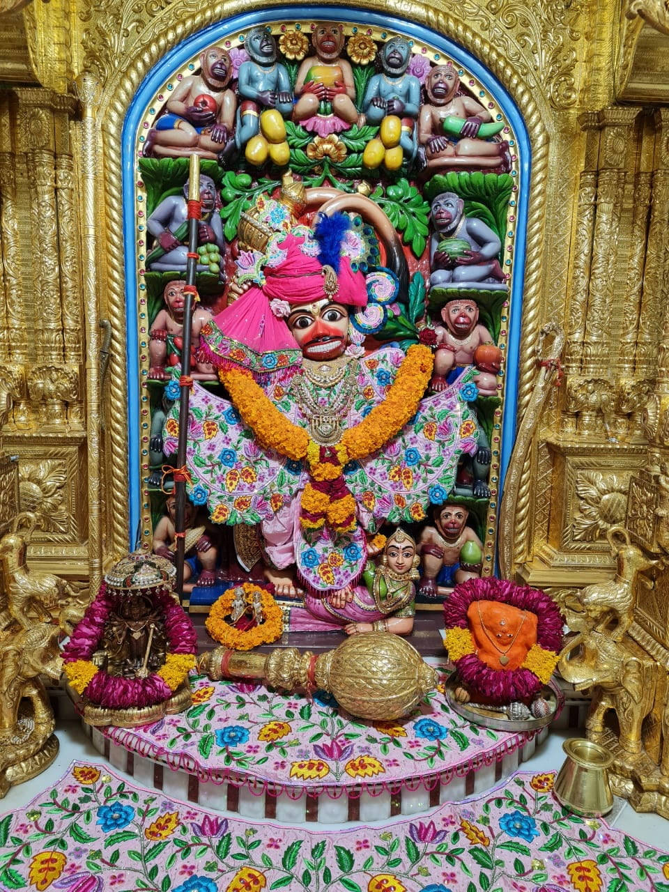 Hindu Temple 桌布 壁紙 — 一尊裝飾鮮豔的印度教神像，飾有鮮花、珠寶，並被金色華麗雕刻和較小的人物所環繞。