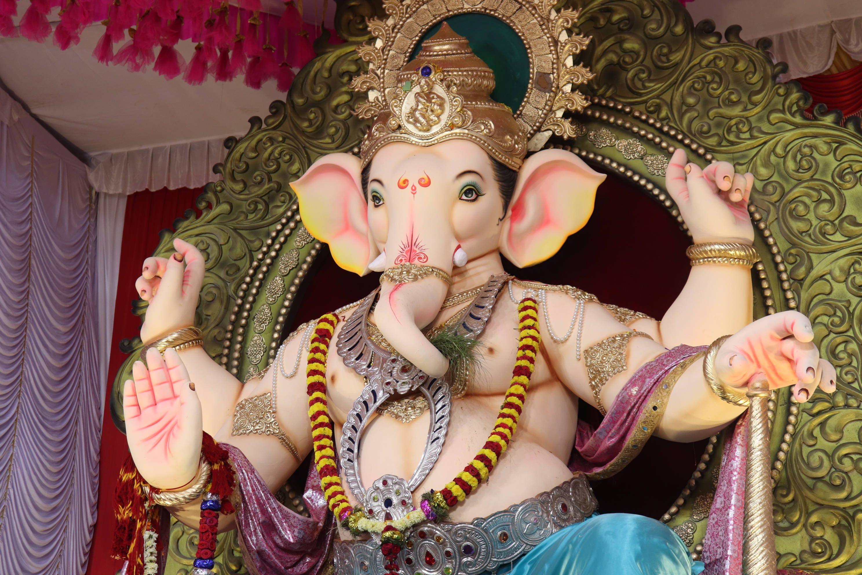 Ganesh 桌布 壁紙 — 一尊裝飾鮮豔的象神雕像，戴著金色皇冠和彩色花環，威嚴地坐在華麗的綠色寶座上。