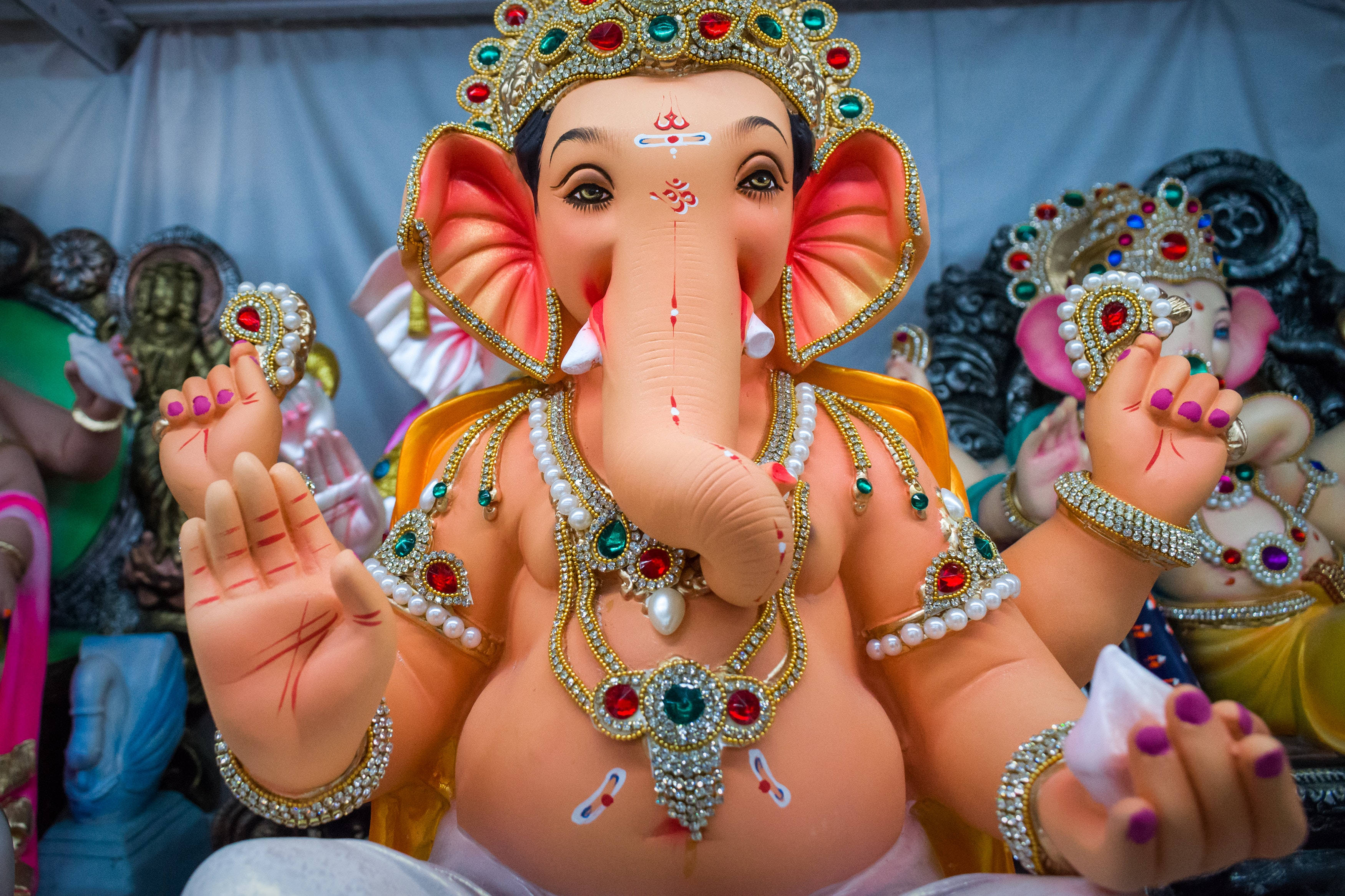 Ganesh Chaturthi 桌布 壁紙 — 一尊裝飾鮮豔的象神雕像，飾有寶石和彩色顏料，在其他節日偶像中顯眼地坐著。