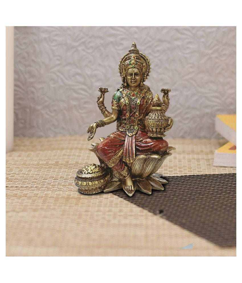 Lakshmi Devi 桌布 壁紙 — 一尊詳細的坐姿印度教女神雕像，身穿紅金服飾，安放在編織墊上，背景是紋理牆壁。