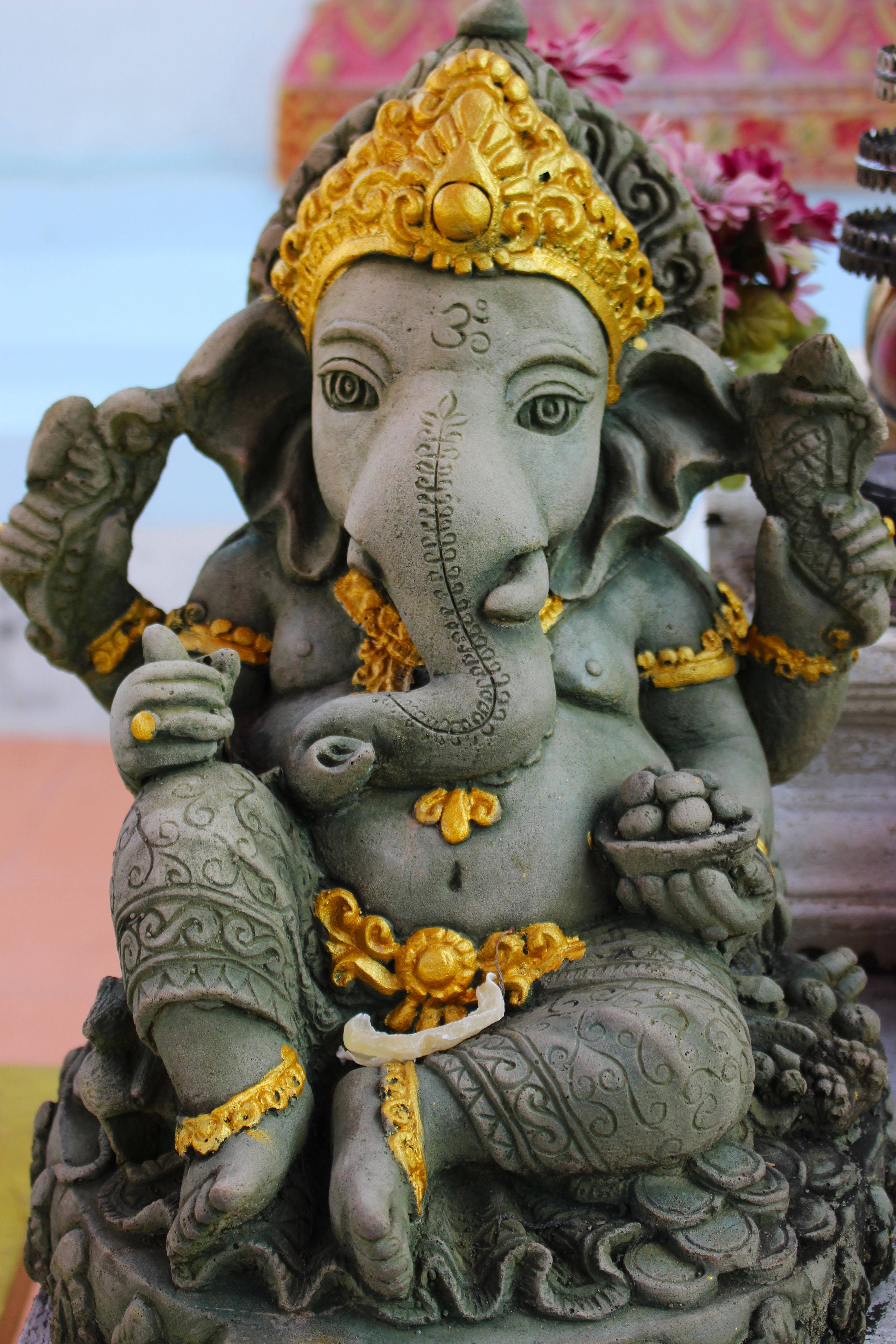 Ganesh 桌布 壁紙 — 一尊詳細的石雕象頭神像，飾有金色裝飾，並在寧靜的寺廟環境中手持象徵性物品。