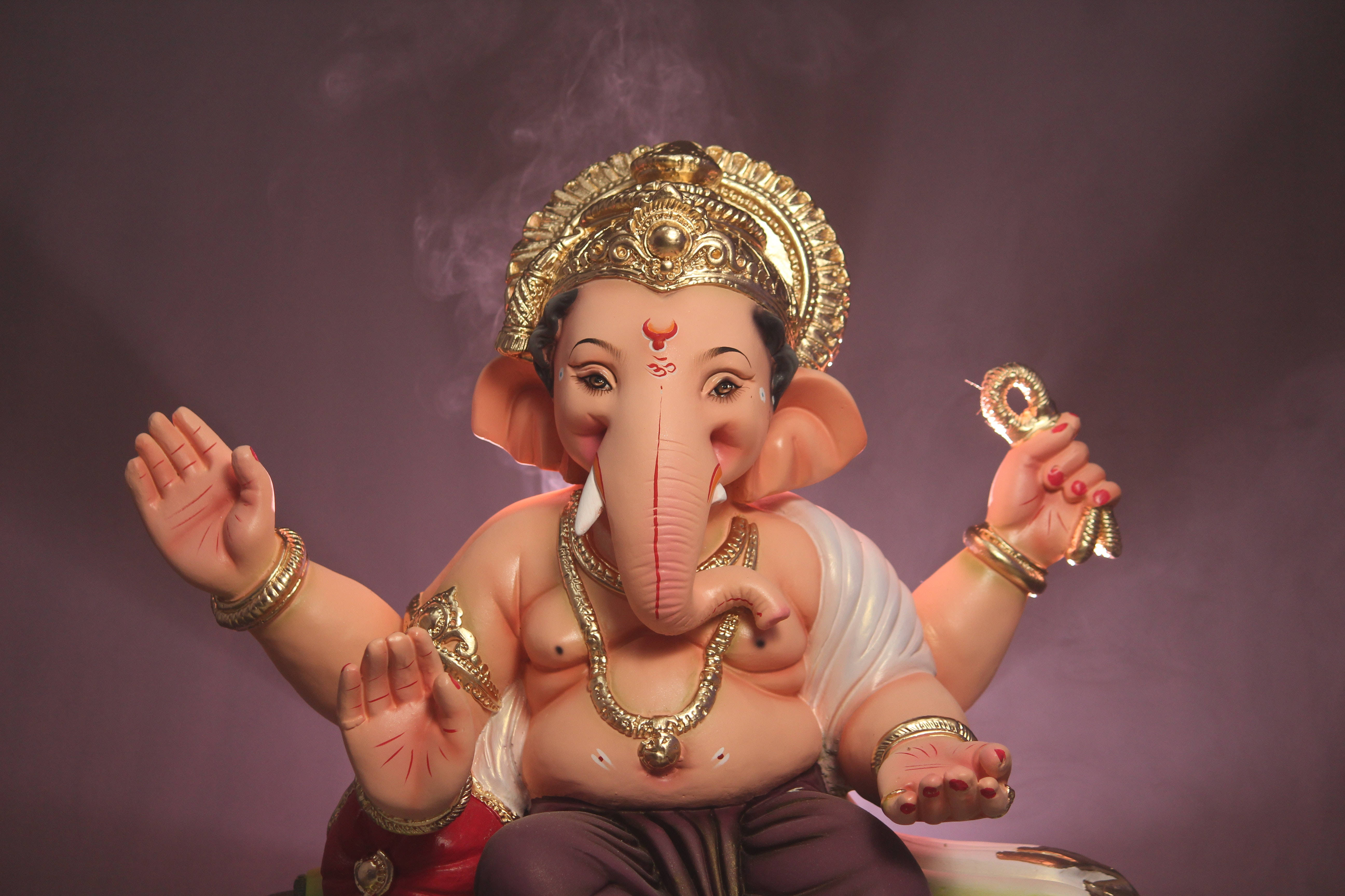 Ganesh Chaturthi 桌布 壁紙 — 一尊詳細的象頭神像，戴著金色王冠和珠寶，坐在煙霧繚繞的紫色背景前。