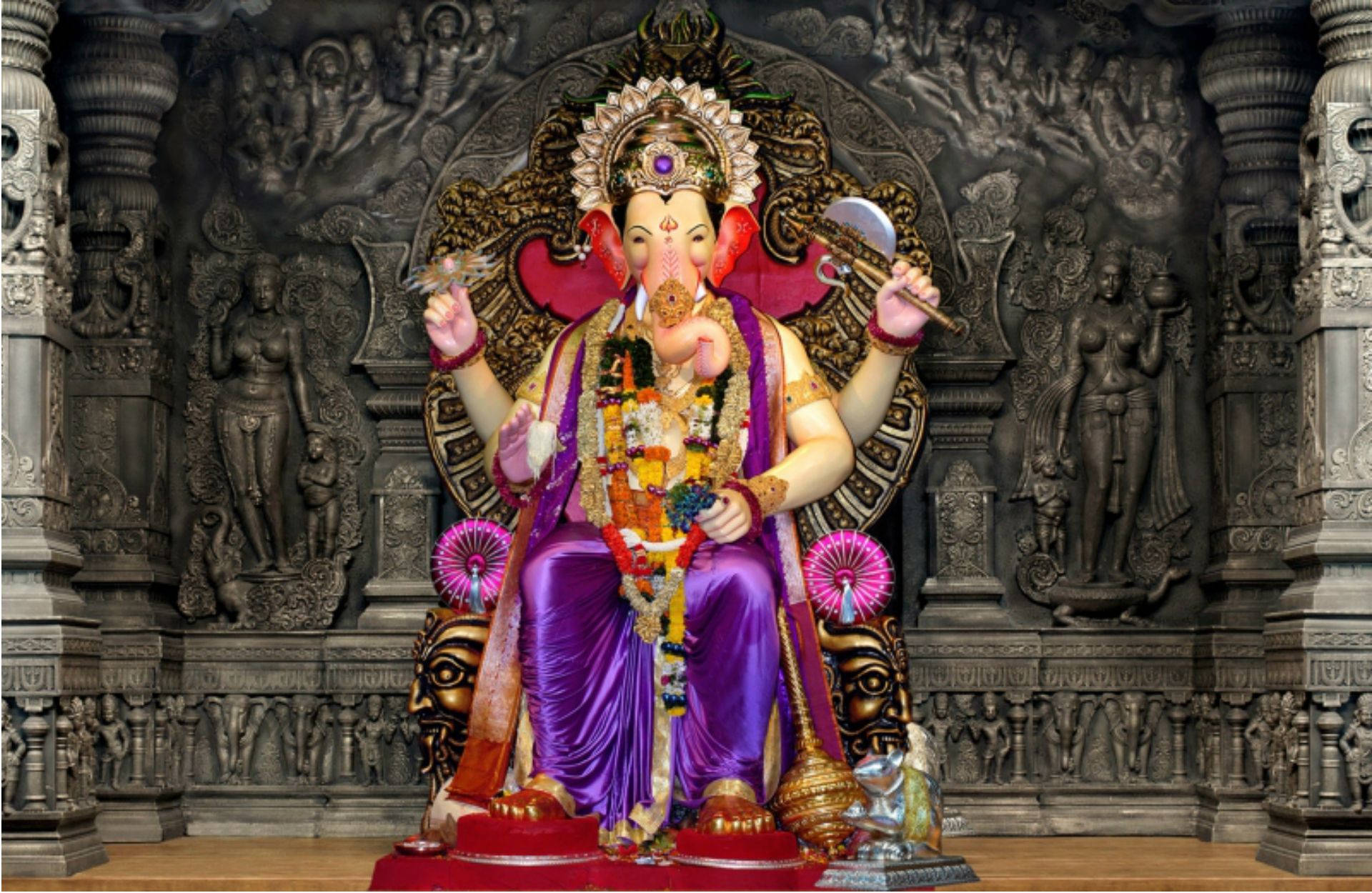 Hindu Temple 桌布 壁紙 — 一尊身穿紫色長袍、飾有鮮花和珠寶的燦爛象神像，威嚴地坐在紅色基座上，位於雕刻精美的寺廟神龕中。