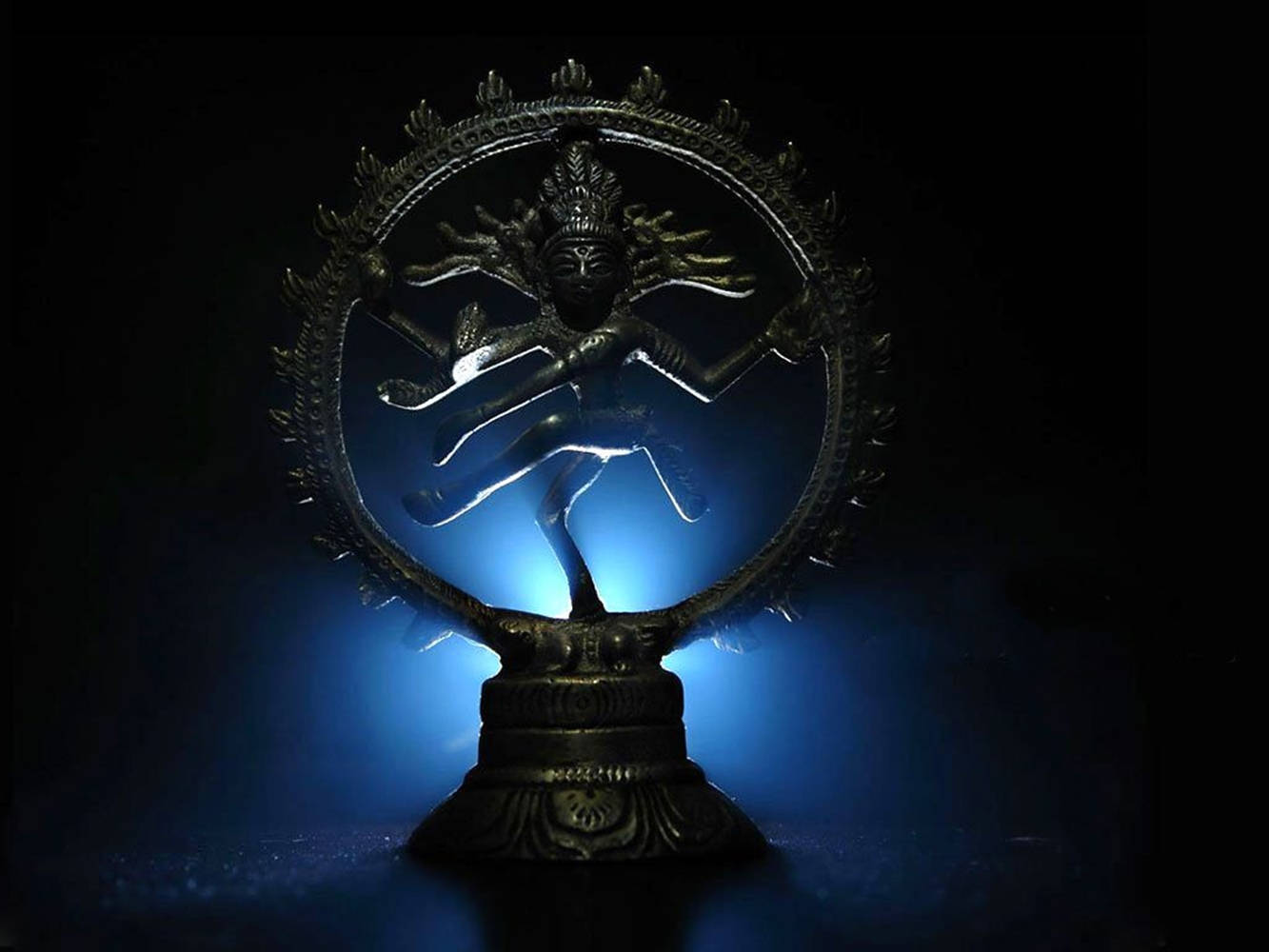 Hindu God 桌布 壁紙 — 一尊金屬濕婆·納塔拉賈雕像在黑暗背景下發出藍色背光，捕捉了毀滅與創造的宇宙之舞。