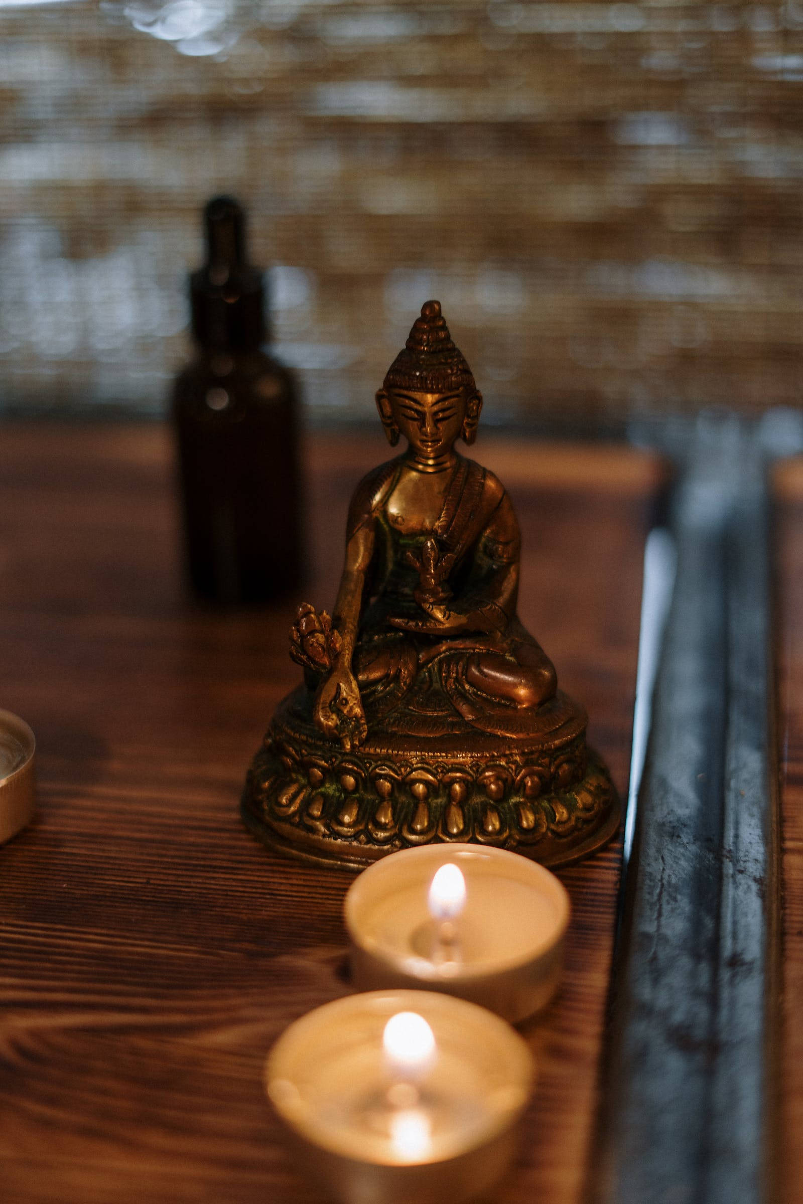 Gautam Buddha 桌布 壁紙 — 一尊金色佛像安詳地坐在木桌上，旁邊是發光的茶燭和香枝，房間光線柔和。