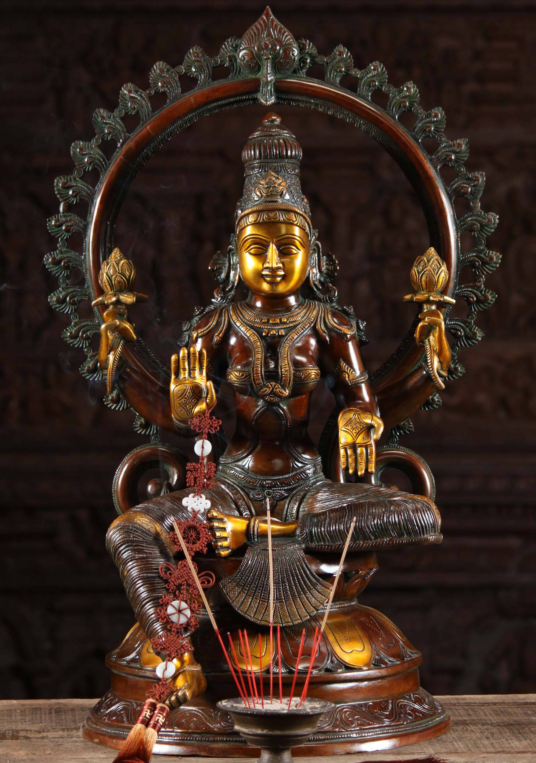 Lakshmi Devi 桌布 壁紙 — 一尊金色四臂印度教神像，帶有精緻的青銅細節，安詳地坐在蓮花寶座上，周圍環繞著香和華麗的雕刻。