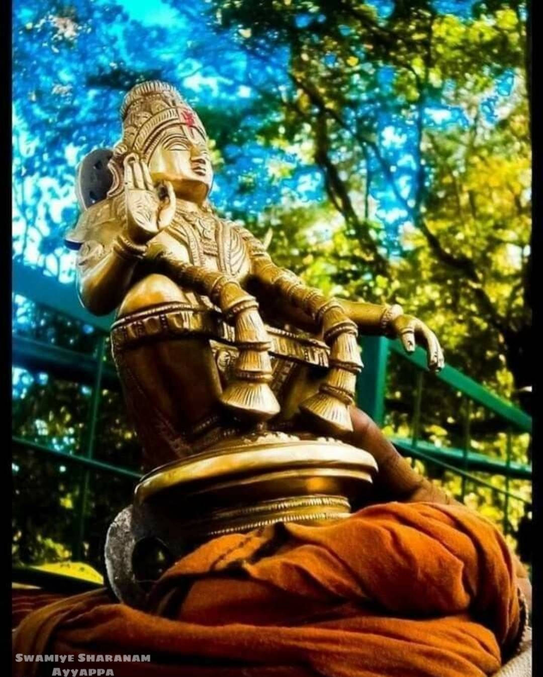 神 桌布 壁紙 — 一尊金色的Ayyappa雕像披著橙色布料，安詳地坐在充滿活力的綠色樹冠下。