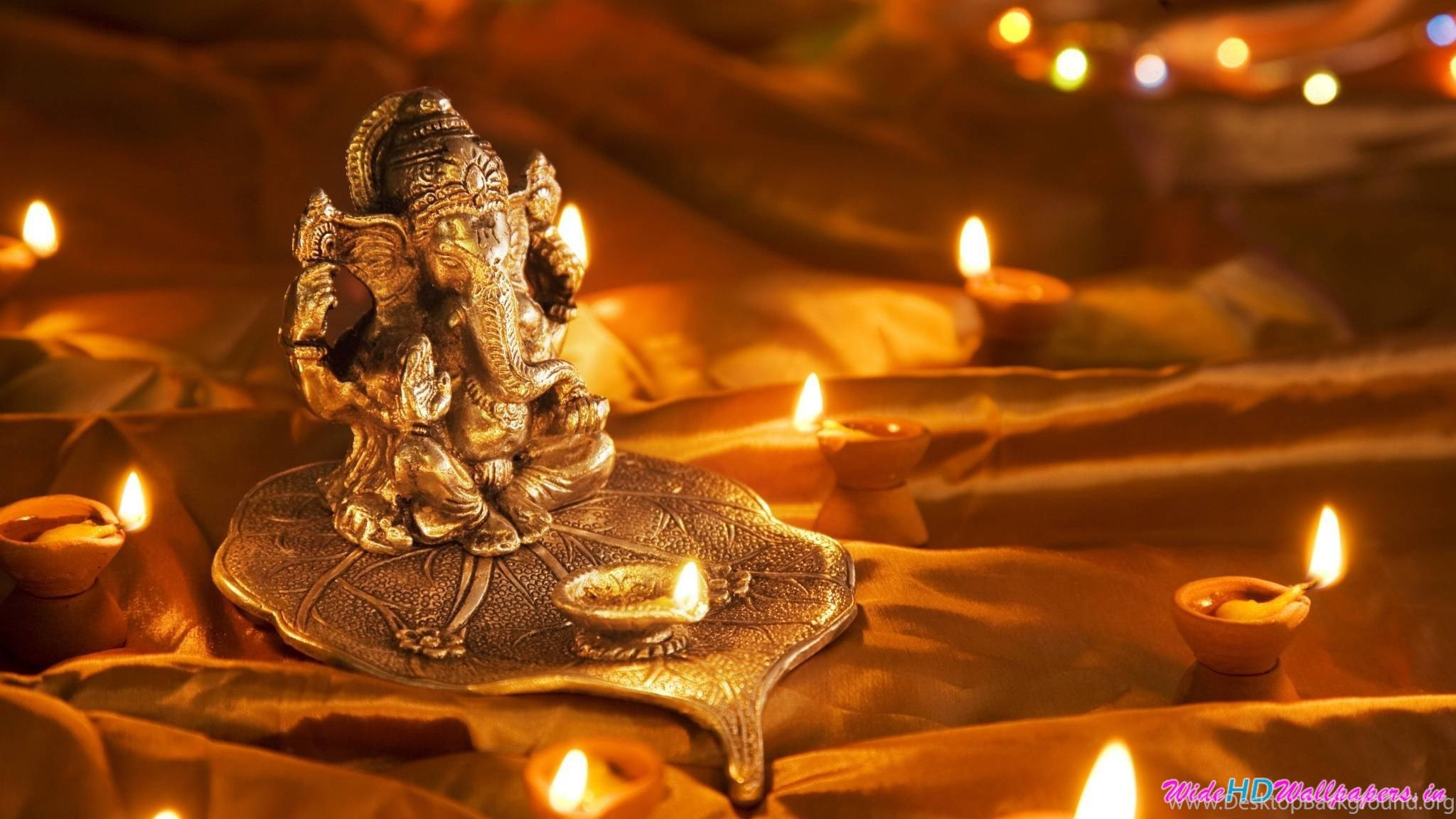 Ganesh 桌布 壁紙 — 一尊金色的Ganesha雕像安詳地坐在一個葉形盤子上，周圍是在垂墜布料上發光的油燈。