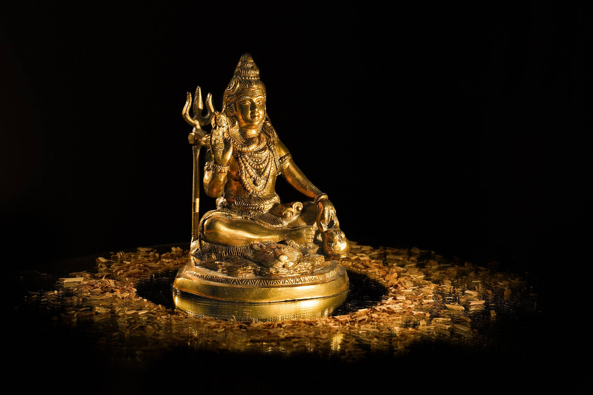 shiv shankar 桌布 壁紙 — 一尊金色的印度教神像安詳地坐在黑色背景上的米粒床上。