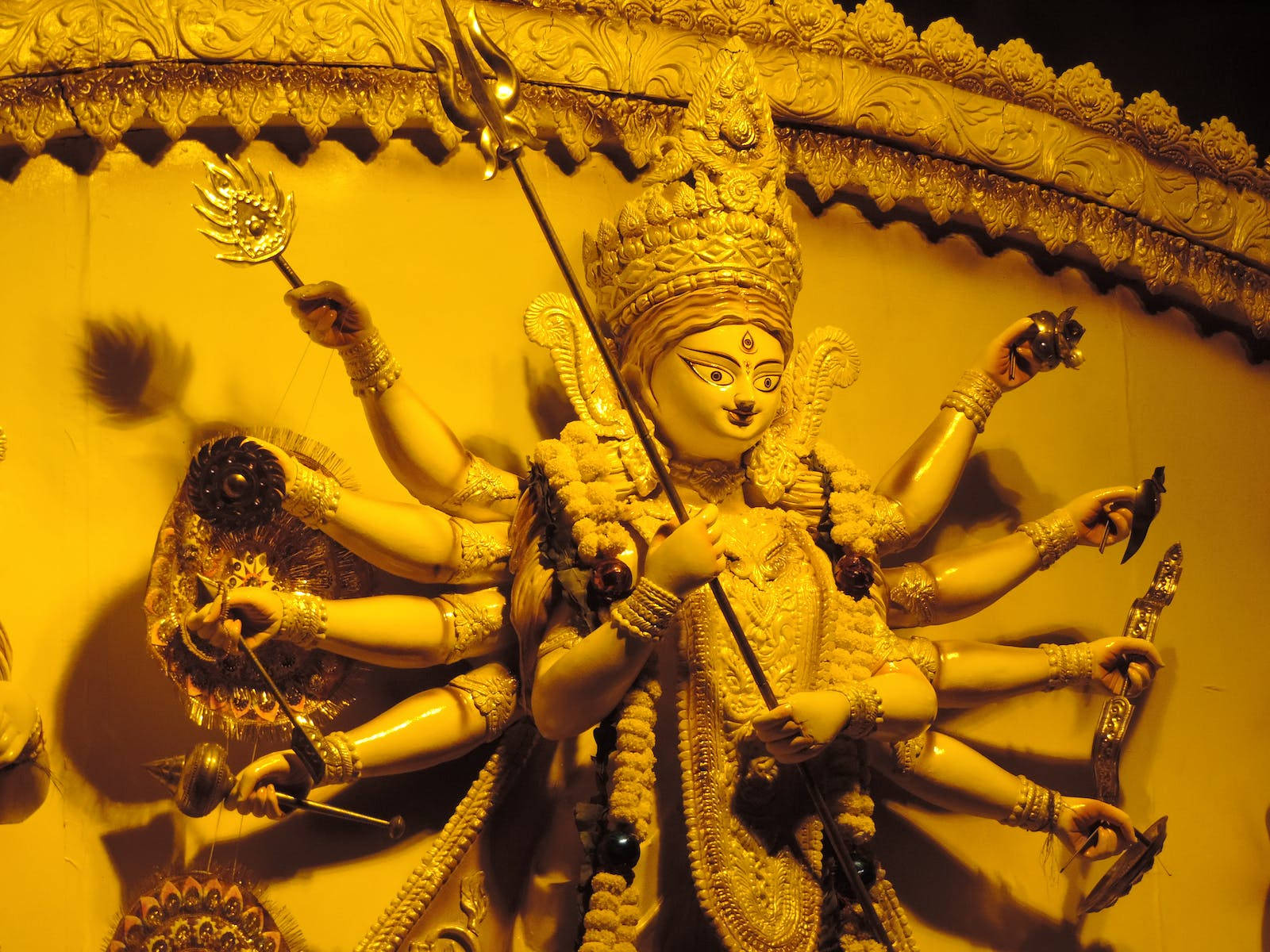 Navratri 桌布 壁紙 — 一尊金色的杜爾迦雕像，多臂手持武器，在華麗的背景前被照亮。
