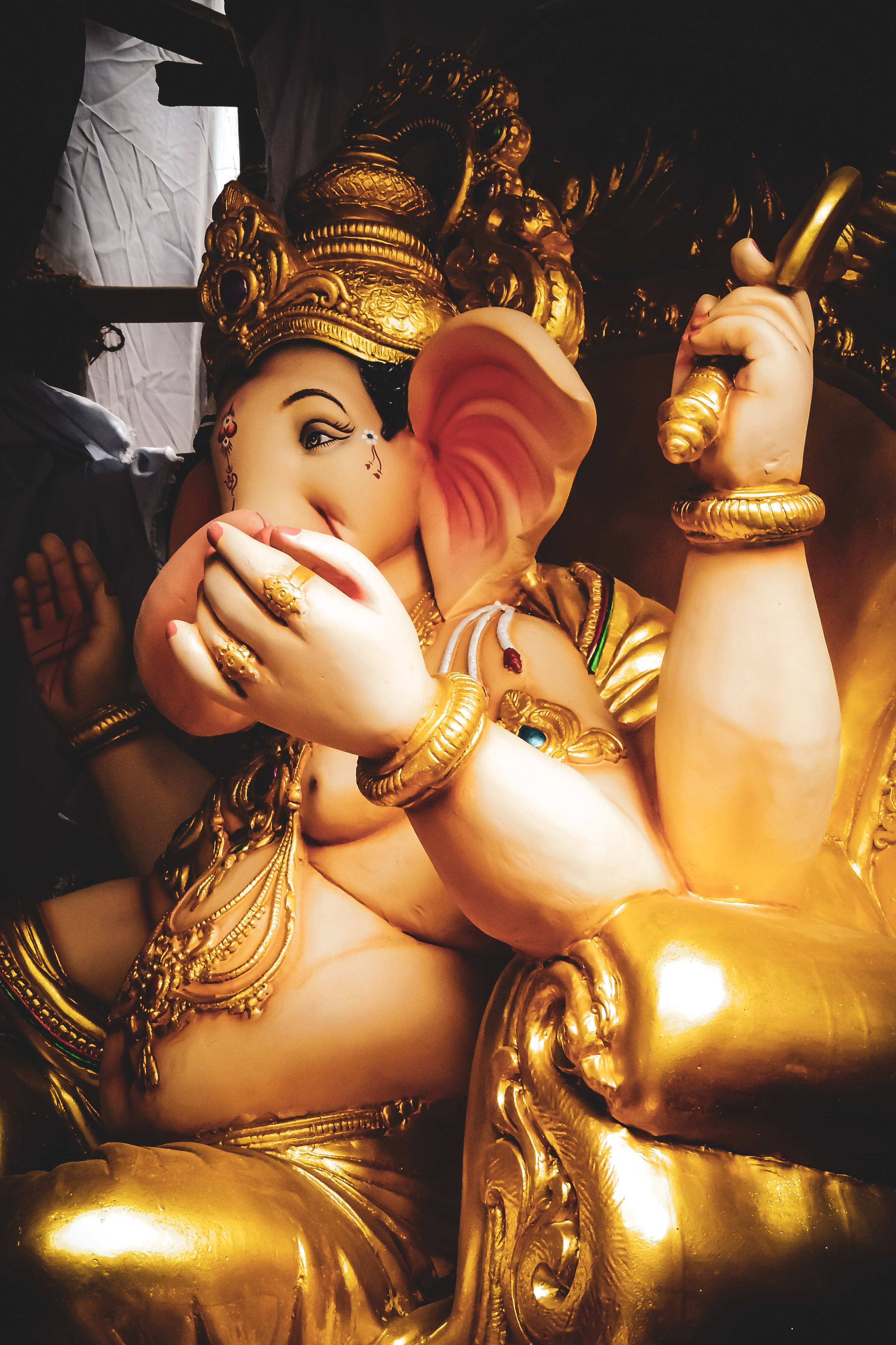 Bappa 桌布 壁紙 — 一尊金色的象神雕像，佩戴精緻珠寶，舉起一隻手，在溫暖的燈光下，以黑暗背景為襯，威嚴地坐著。