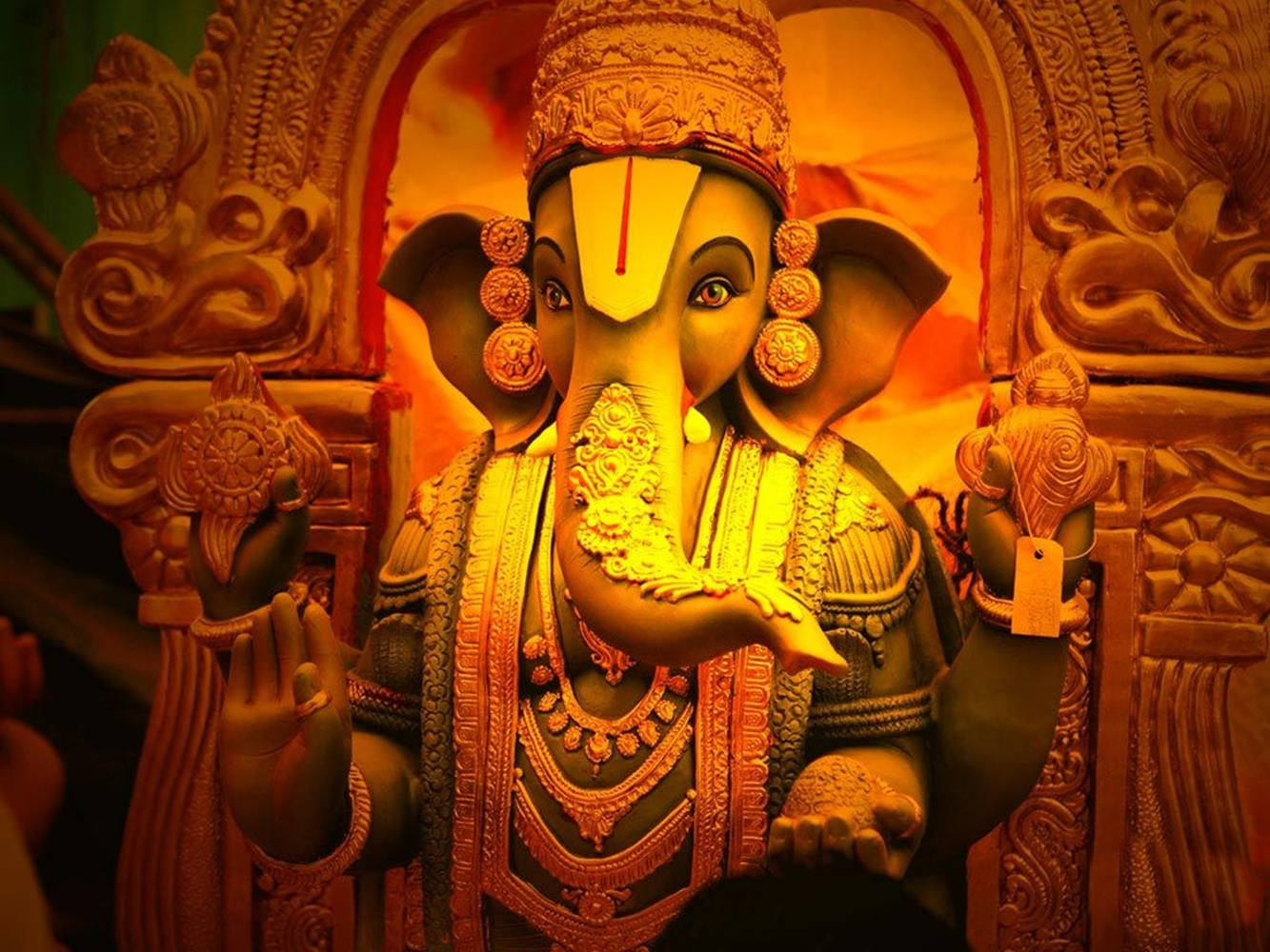 Ganesh 桌布 壁紙 — 一尊金色的象頭神像，飾有精緻珠寶，坐在華麗的寶座上，沐浴在溫暖的光芒中。