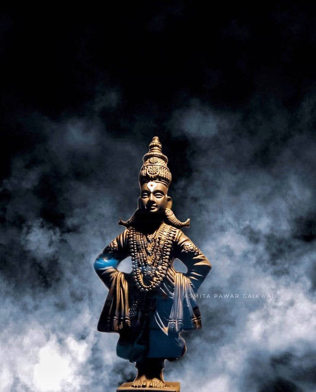 Indian 桌布 壁紙 — 一尊金色神像在旋轉的烏雲中擺出姿勢，戲劇性的燈光突顯了複雜的珠寶和皇冠細節。