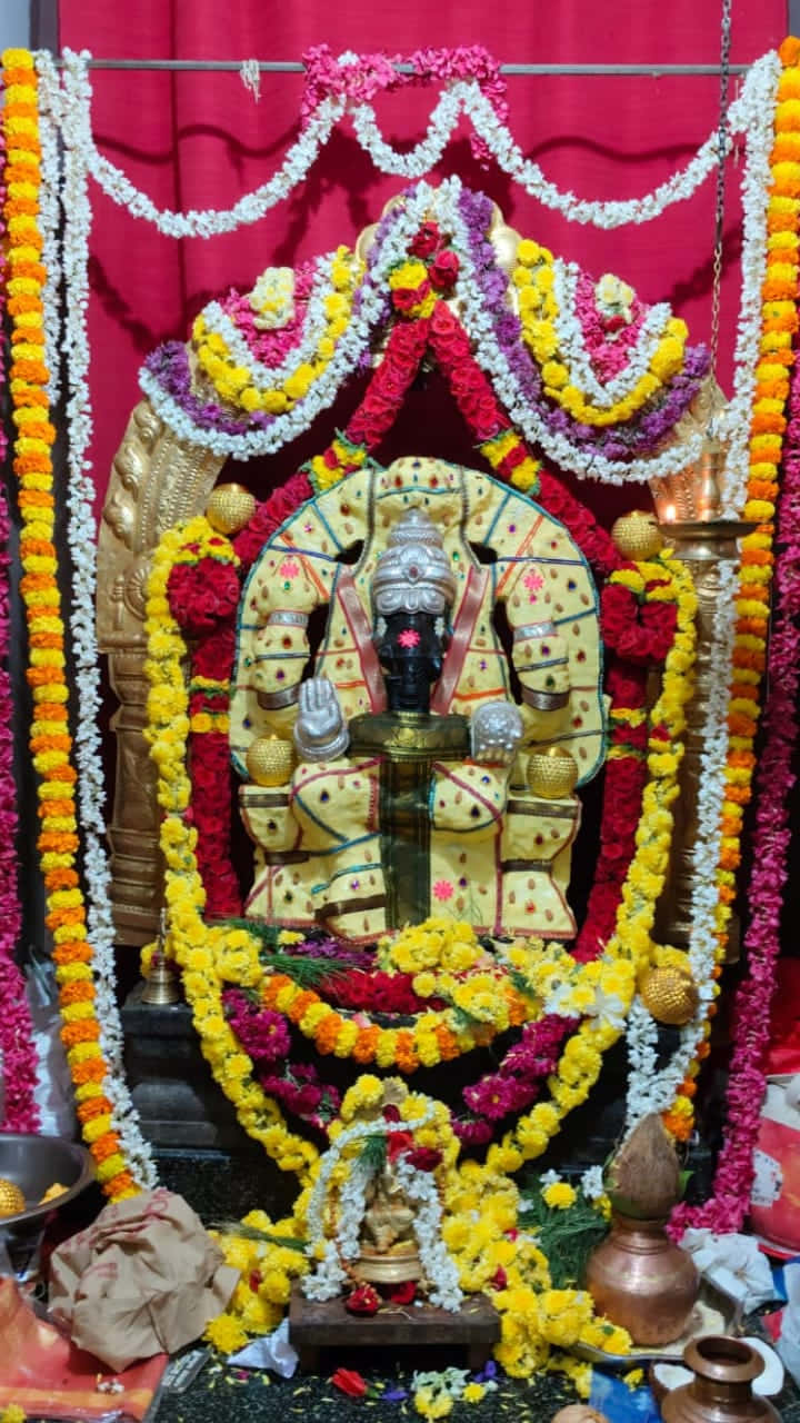 Ganesh 壁紙 — 一尊金色神像飾以鮮豔的黃、紅、白花環，坐在寺廟的紅色帷幕下。