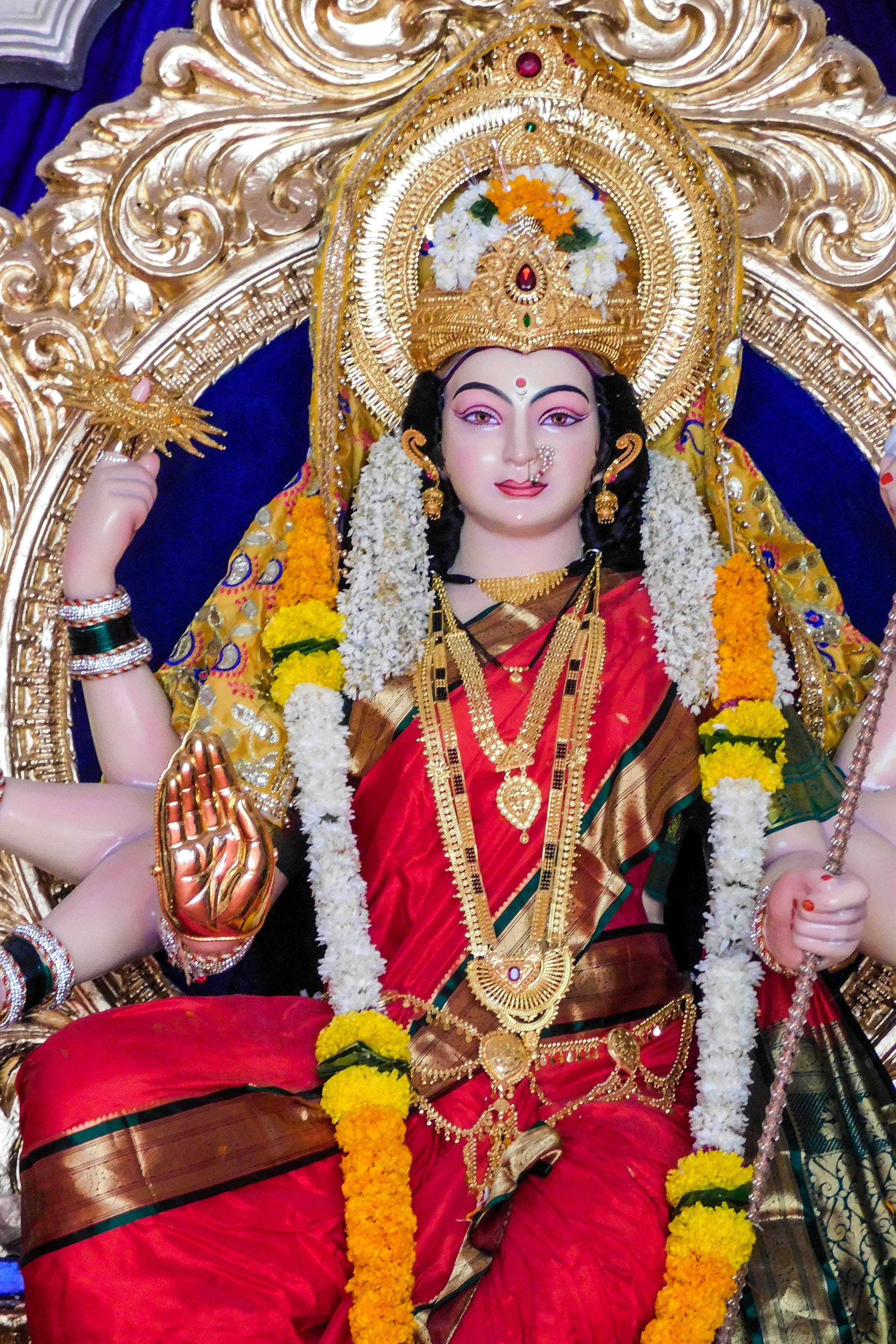Mata Rani 桌布 壁紙 — 一尊閃耀的印度教女神雕像，身披紅絲綢和黃金珠寶，坐在裝飾華麗的金色寶座上，周圍環繞著花環。