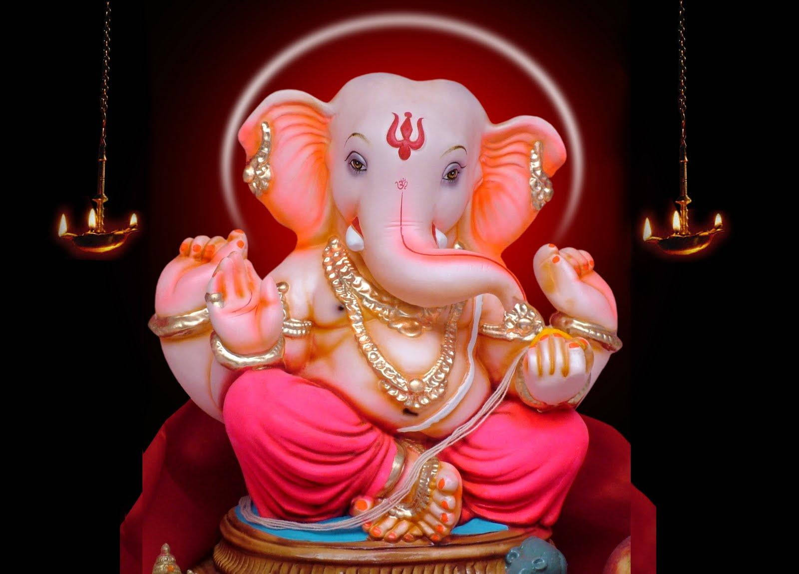 Ganesh 桌布 壁紙 — 一尊閃耀的粉紅色象神雕像，飾有黃金珠寶，安詳地坐在紅色基座上，兩旁是發光的油燈，背景漆黑。