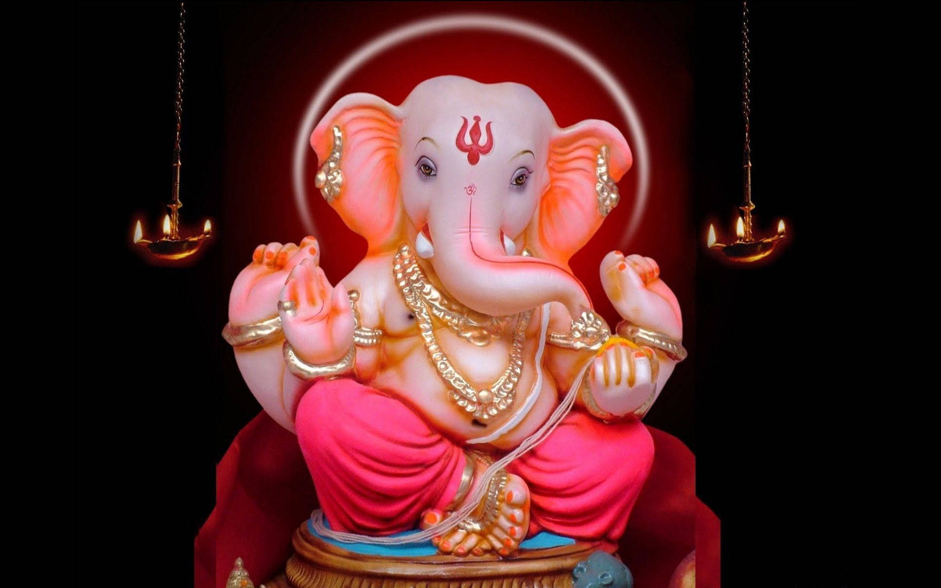 ganpati HD 桌布 壁紙 — 一尊閃耀的粉紅色象頭神雕像，飾有金色珠寶，安詳地坐在紅色基座上，兩旁是發光的油燈，背景漆黑。