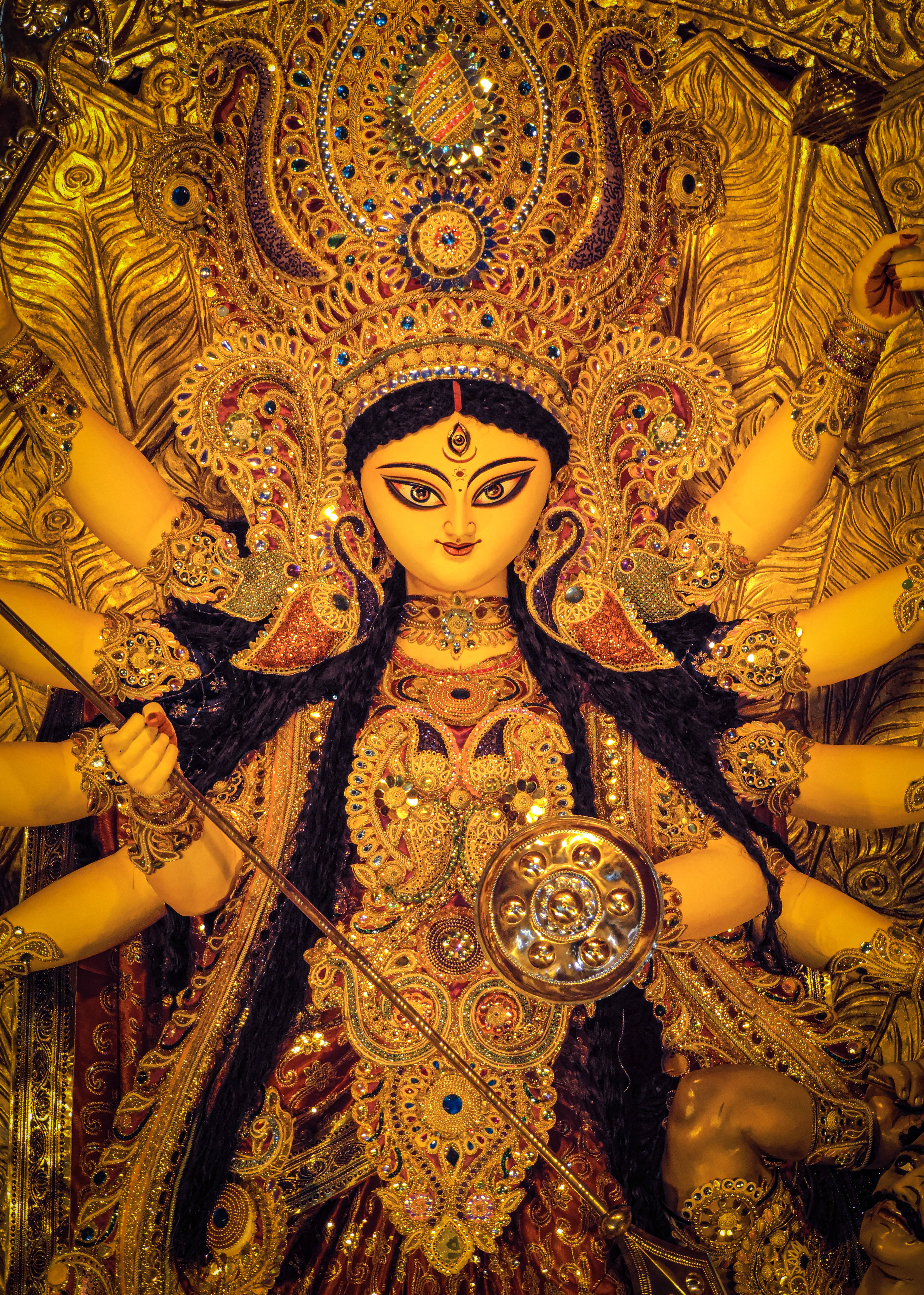 Durga 桌布 壁紙 — 一尊閃耀的金色杜爾迦雕像，多臂佩戴精緻珠寶並手持武器，背景為相配的華麗裝飾。